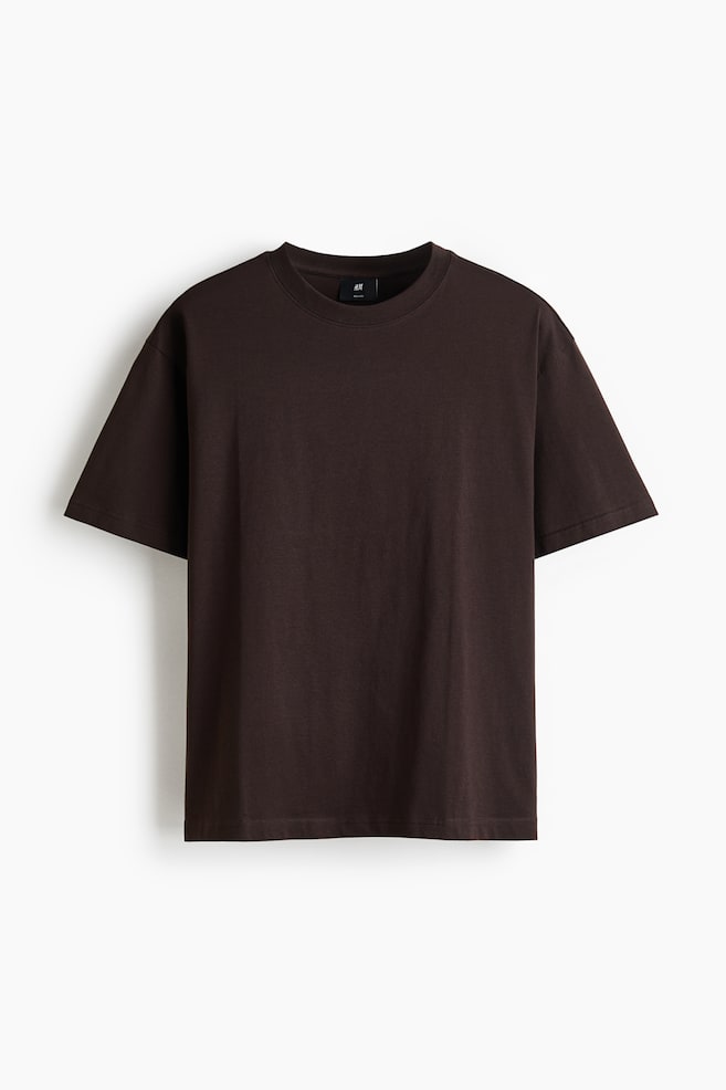 A dark brown t-shirt is showcasing its front view, featuring a round, ribbed neckline and dropped shoulders. It displays a straight-cut hem, offering a relaxed fit for a casual silhouette. - 1