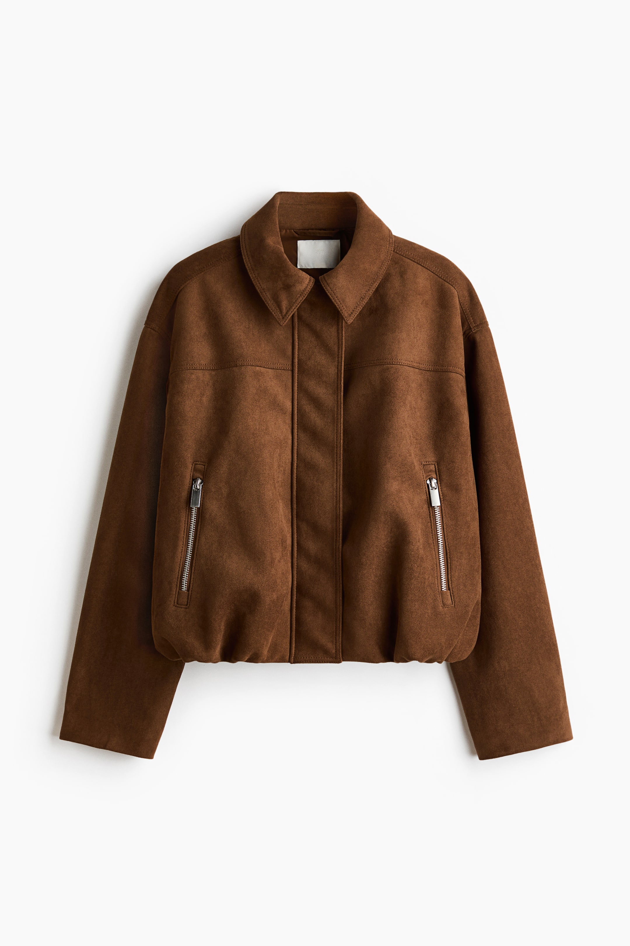 Ver imagen más grande: Una chaqueta marrón está de frente, mostrando una textura similar a la gamuza, un cuello en punta y un panel frontal central con costuras diagonales flanqueadas por costuras verticales. Dos bolsillos con cremallera están situados en la parte inferior delantera, y un dobladillo elástico forma la base de la chaqueta.