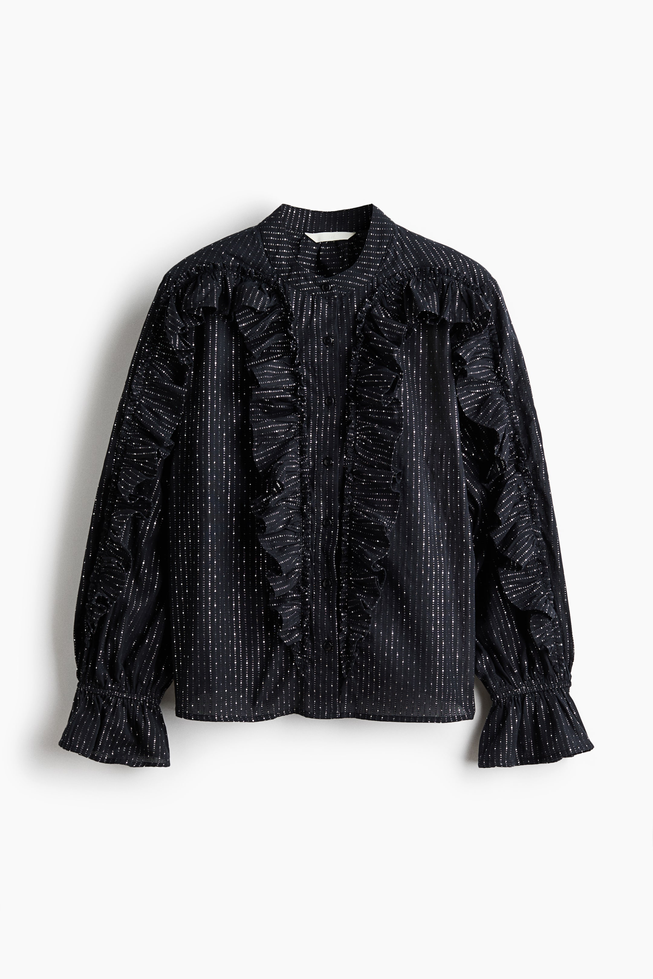 Agrandir l'image: Un chemisier noir est présenté de face, avec un col montant et une patte de boutonnage devant. Le chemisier est orné de rayures verticales en paillettes argentées et est agrémenté de volants encadrant la patte de boutonnage, sur les épaules, et détaillant les manches longues qui se terminent par des poignets à volants.