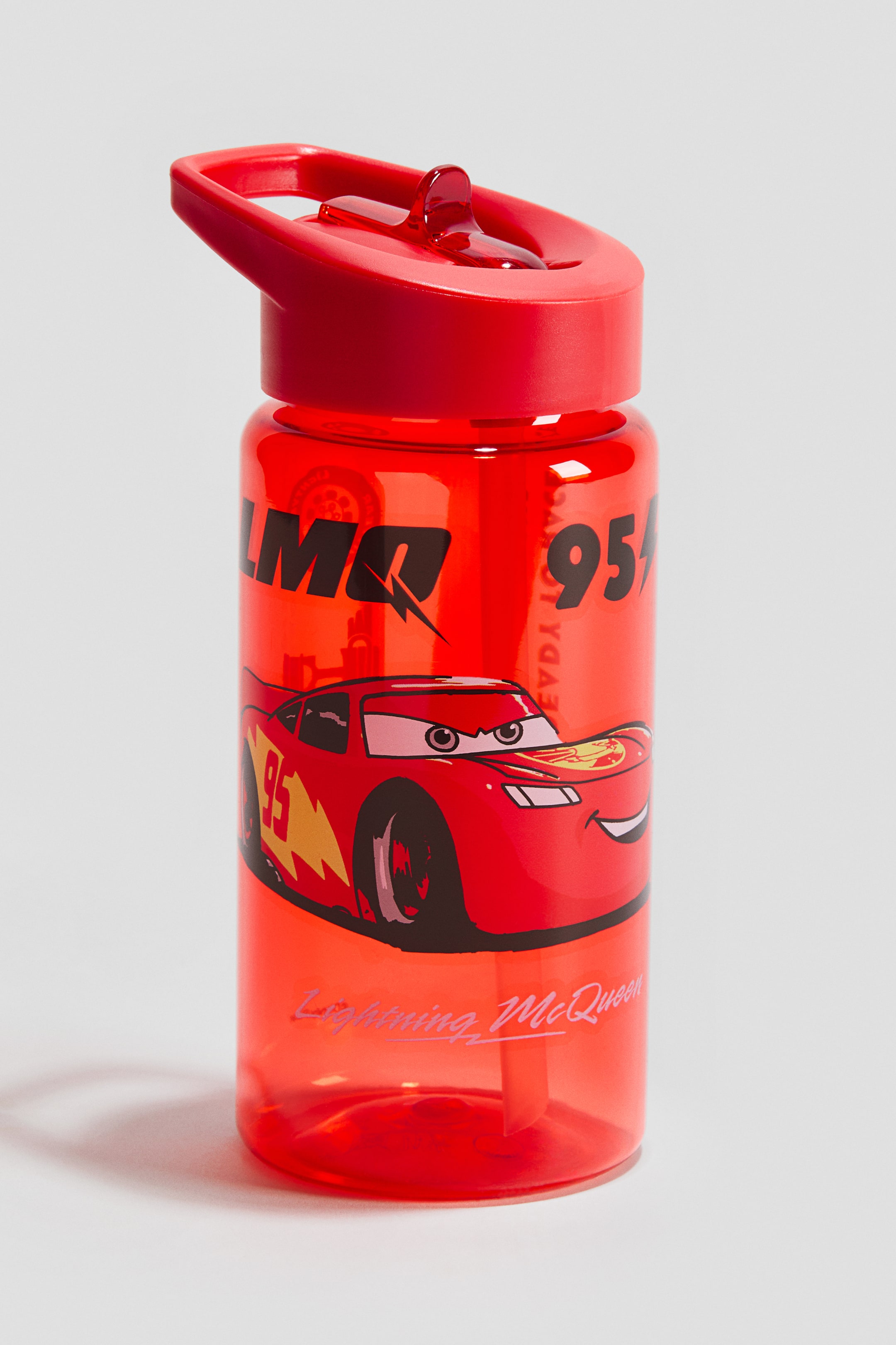 View larger image: A transparent red plastic water bottle features a print of Lightning McQueen facing forward, adorned with the number 95. It comes with a red lid that includes an integrated handle and an open spout, with a straw extending inside the bottle.