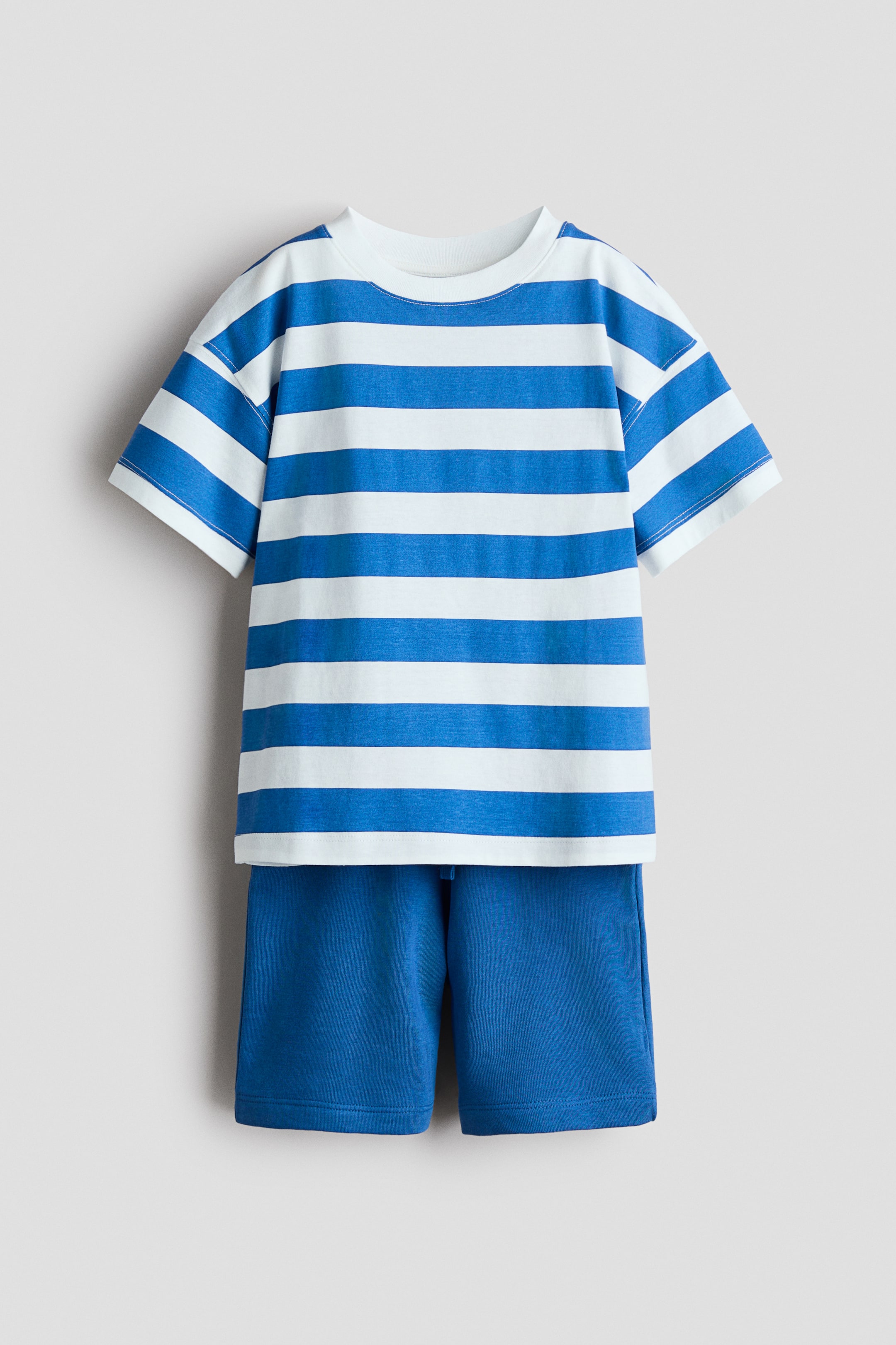 View larger image: A front-facing set showcases a white and blue striped T-shirt paired with solid blue shorts. The T-shirt features a round, ribbed neckline, dropped shoulders, and a straight-cut hem, while the shorts boast an elasticated, drawstring waist and diagonal side pockets.