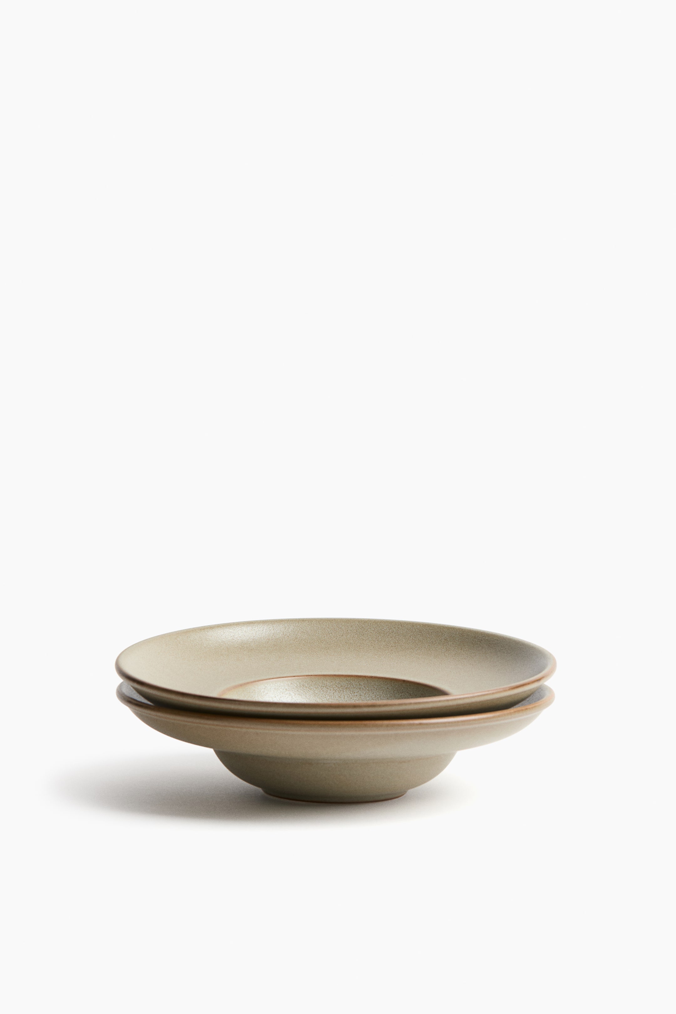 View larger image: Two small, deep stoneware plates feature a reactive glaze, creating variegated coloring and giving each plate a unique appearance. They are subtly stacked, with the top plate resting inside the bottom one, presented at a front angle.