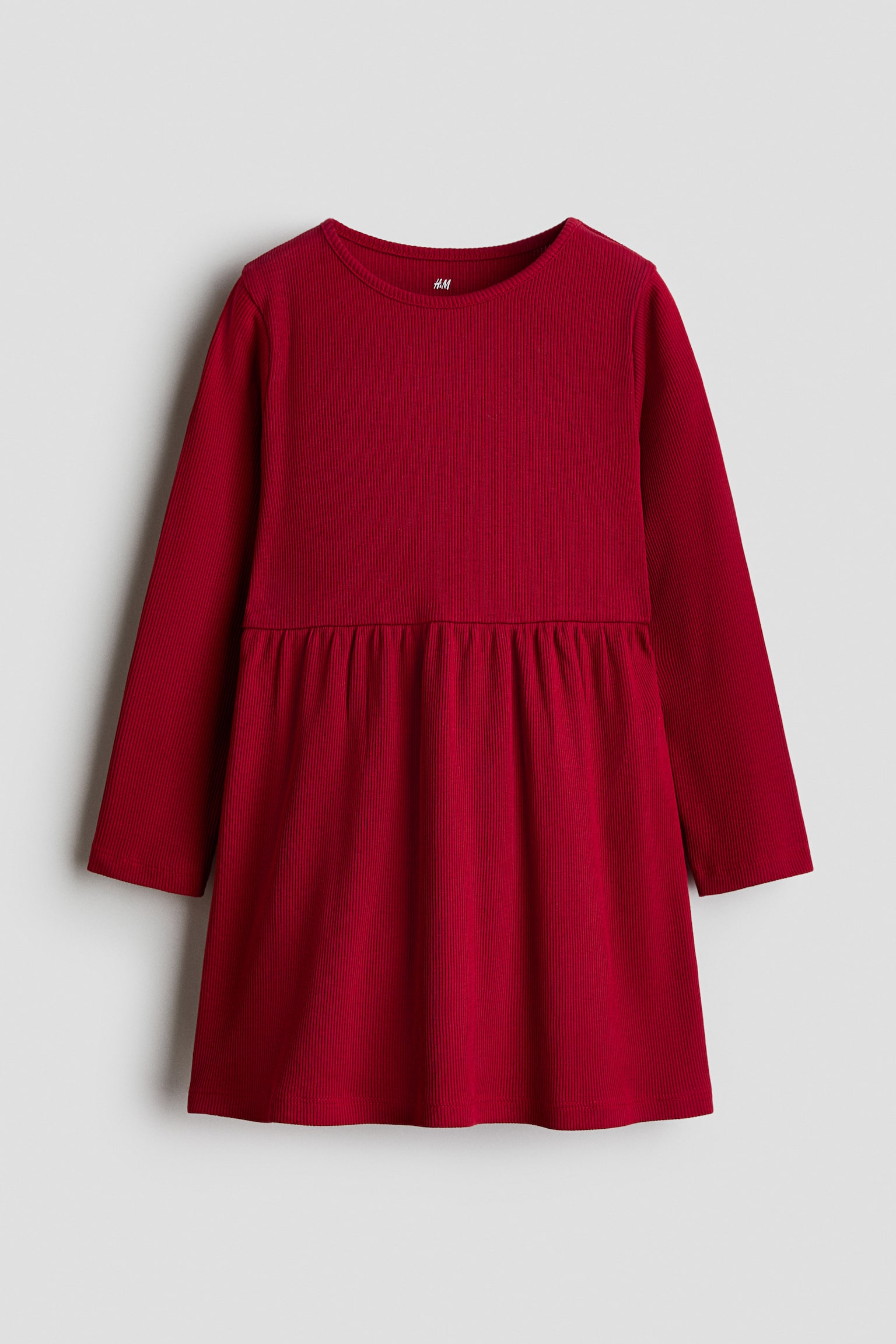 Une robe Ã  manches longues en jersey de coton cÃ´telÃ© rouge est prÃ©sentÃ©e de face, avec un col rond, des manches longues et une couture froncÃ©e Ã  la taille qui sâouvre sur une jupe lÃ©gÃ¨rement Ã©vasÃ©e.
