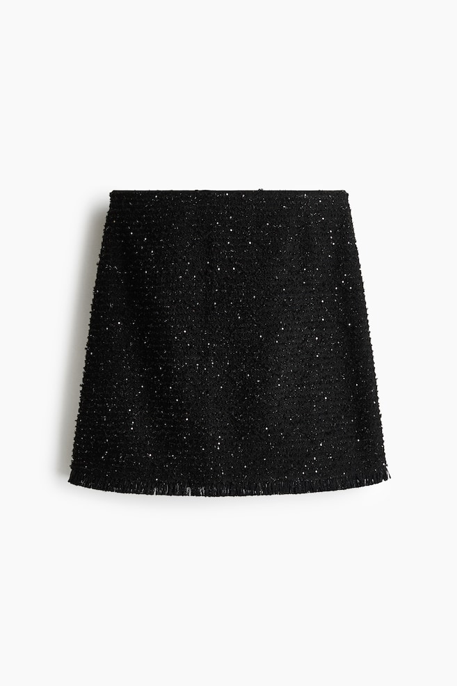 Ein schwarzer Tweed-Minirock ist von vorne zu sehen und zeigt einen strukturierten Stoff mit eingewebten, kleinen, schimmernden Pailletten. Der Rock präsentiert eine definierte A-Linie und wird mit einem zarten Fransensaum abgeschlossen. - 1