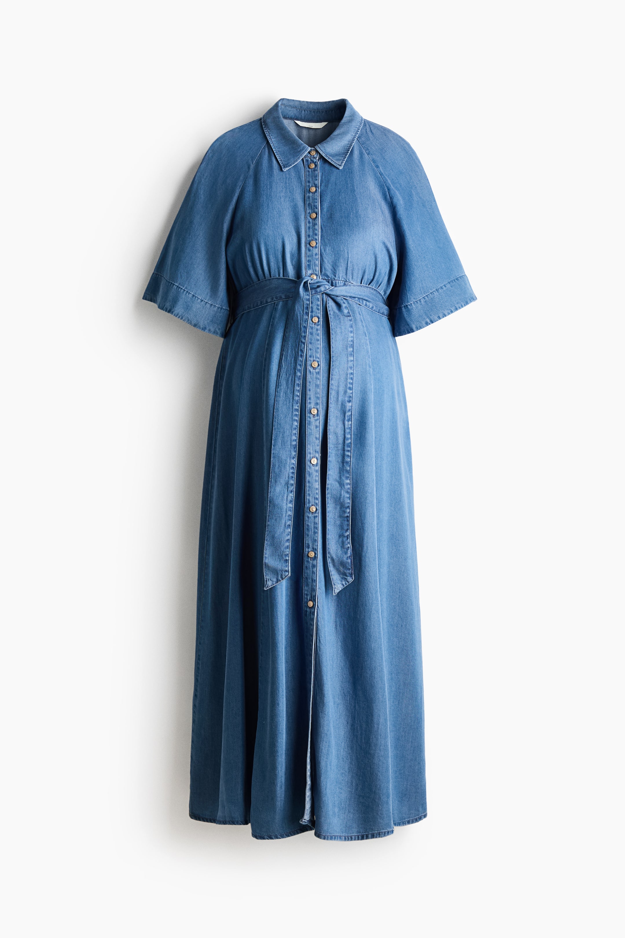 Agrandir l'image: Une robe mi-mollet en denim doux lyocell se présente de face, avec un col et des boutons brillants descendant sur le devant. Elle est conçue avec des manches raglan longueur coude, une élastication à l'arrière de la taille, une large ceinture à nouer à l'avant, et une jupe évasée.