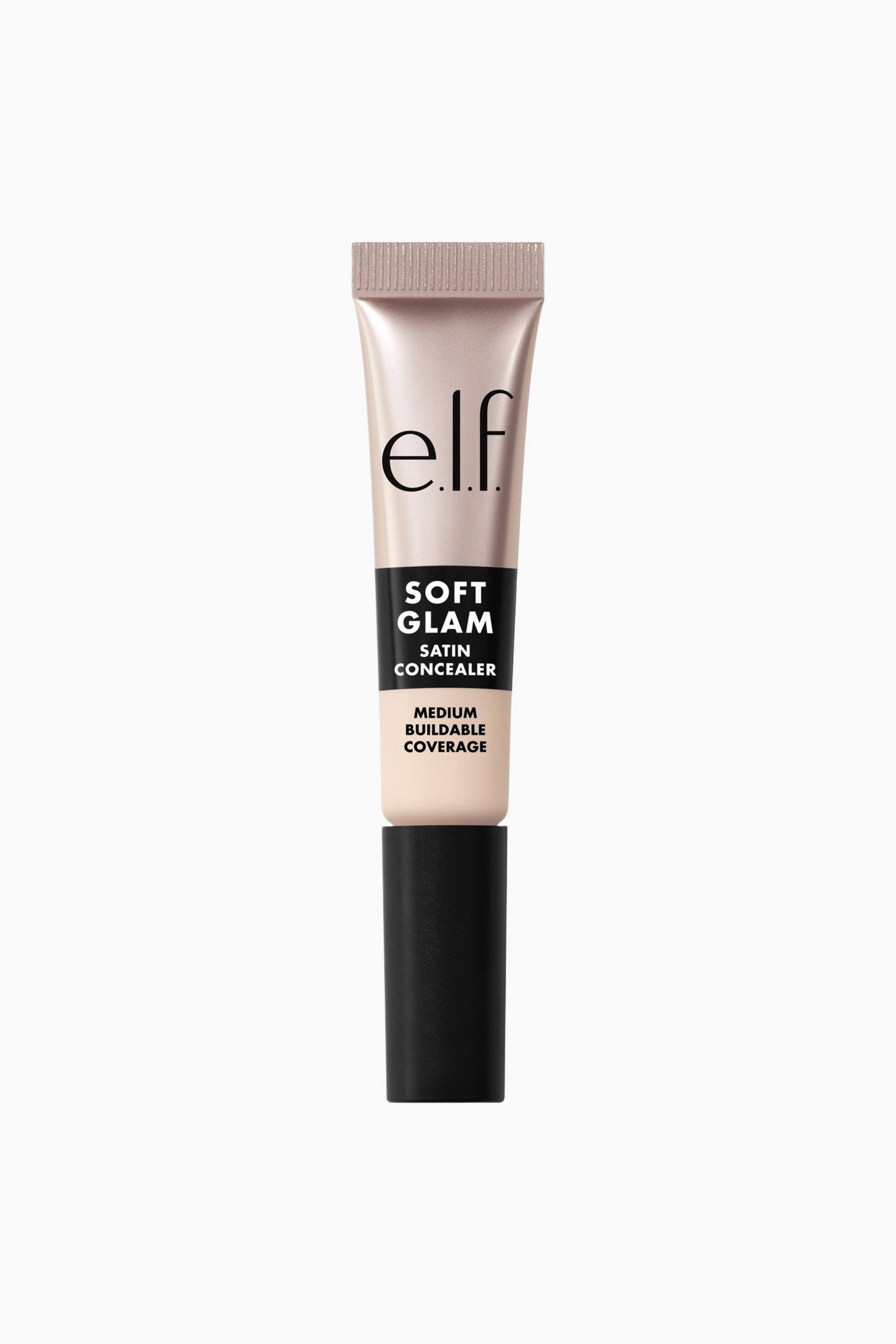 Vis større bilde: En e.l.f. Soft Glam Satin Concealer-tube står oppreist og vender framover. Tuben viser en lys ferskenaktig beige toppseksjon med "e.l.f."-logoen og teksten "Soft Glam Satin Concealer" og "Medium Buildable Coverage", som går over i en lysere beige nederste del, og er dekket av et matt svart lokk.