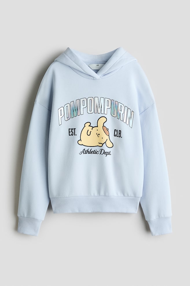 Jasnoniebieska bluza z kapturem o oversizeâowym kroju jest ustawiona przodem, prezentujÄc kaptur typu wrap, obniÅ¼onÄ liniÄ ramion oraz prÄÅ¼kowane wykoÅczenie przy mankietach i u doÅu. Na piersi znajduje siÄ nadrukowana grafika przedstawiajÄca postaÄ z kreskÃ³wki Pompompurin, pod Åukowym napisem âPOMPOMPURINâ i nad napisem âAthletic Dept.â zapisanym odrÄcznie. - 1