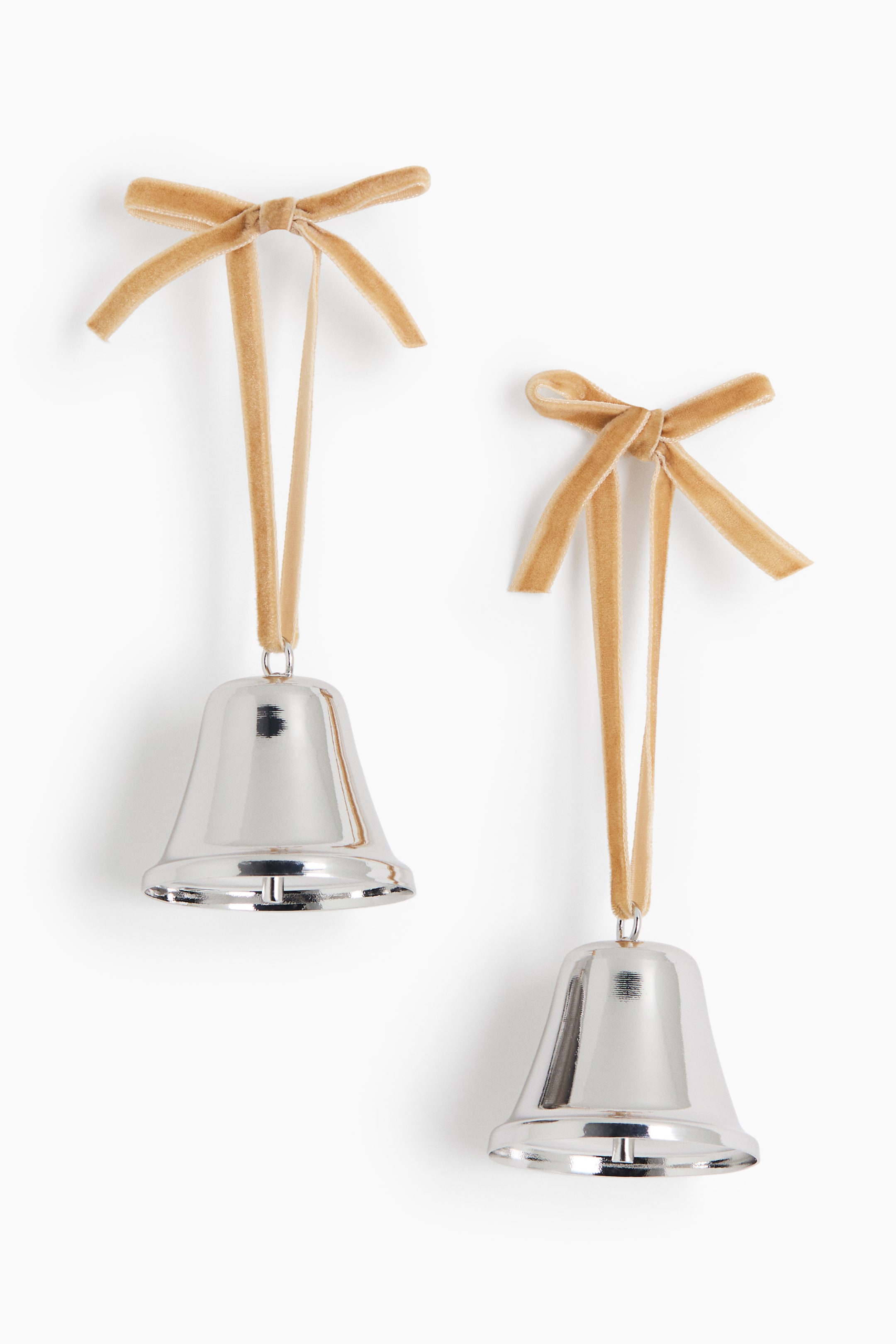 View larger image: Two polished silver-toned bell ornaments are hanging facing the front, each suspended by a light beige velvet ribbon tied into a bow at the top. The bells feature a highly reflective metallic finish with visible inner clappers.