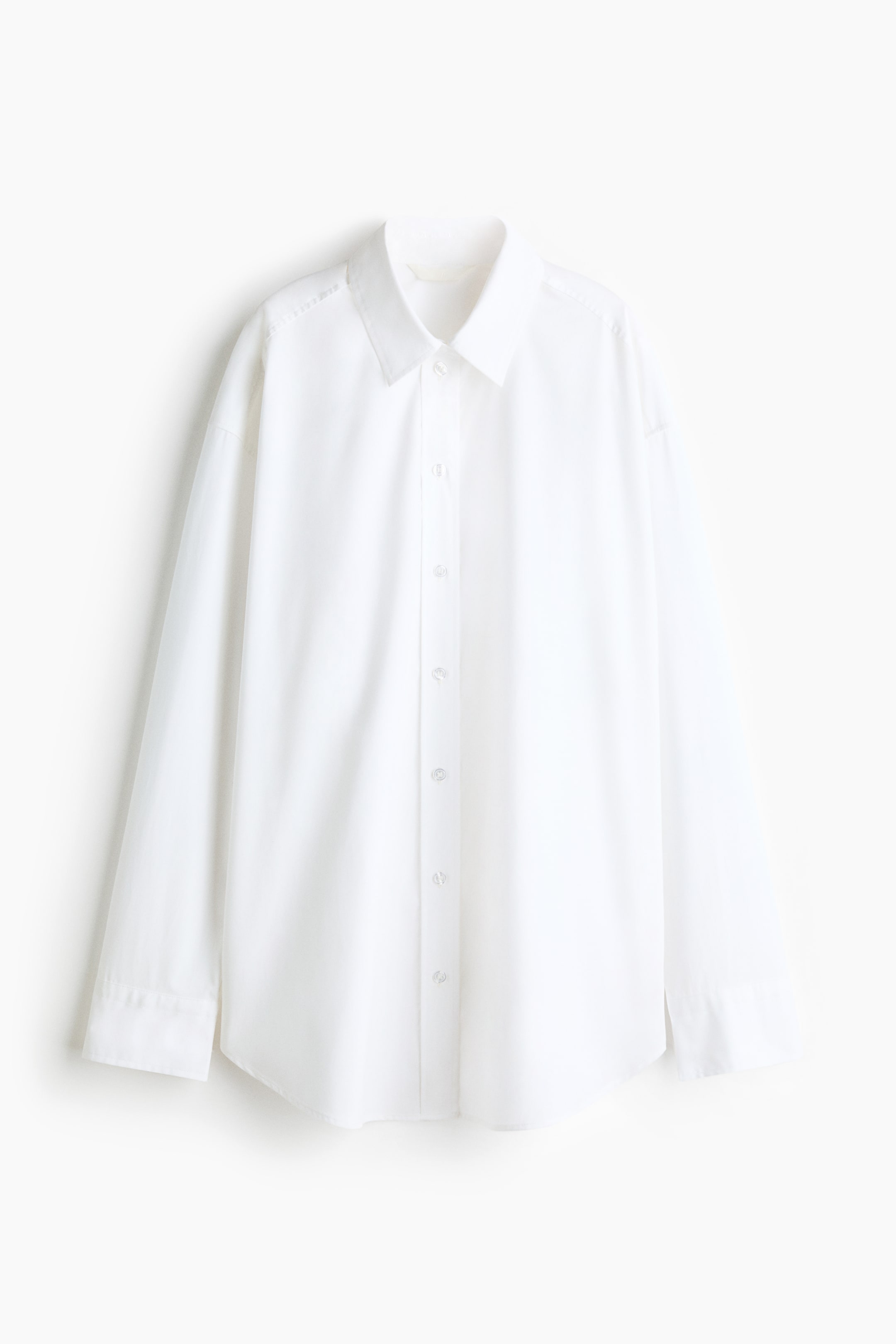 View larger image: An oversized white shirt is shown from the front, featuring a classic collar, a central button-front placket, and long sleeves with button cuffs. The shirt has a relaxed, loose silhouette with dropped shoulders and a rounded hem.