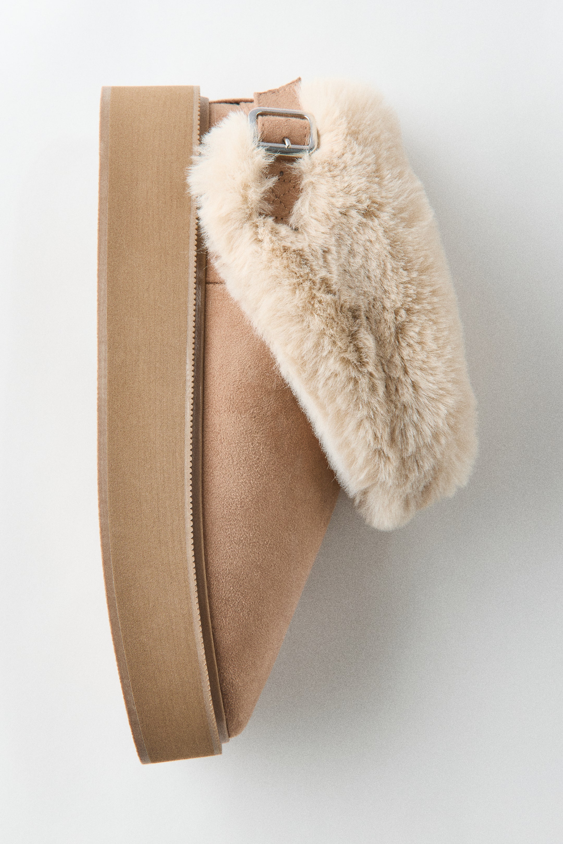 Größeres Bild anzeigen: Ein hellbrauner Flatform-Stiefel ist in der Seitenansicht zu sehen und zeigt sein weiches Obermaterial aus Kunstveloursleder sowie die dicke, tonale Flatform-Sohle. Der Stiefel verfügt über einen umgeschlagenen Schaft mit flauschigem, cremefarbenem Kunstfellfutter und einen verstellbaren Fersenriemen mit silberfarbener Metallschnalle.