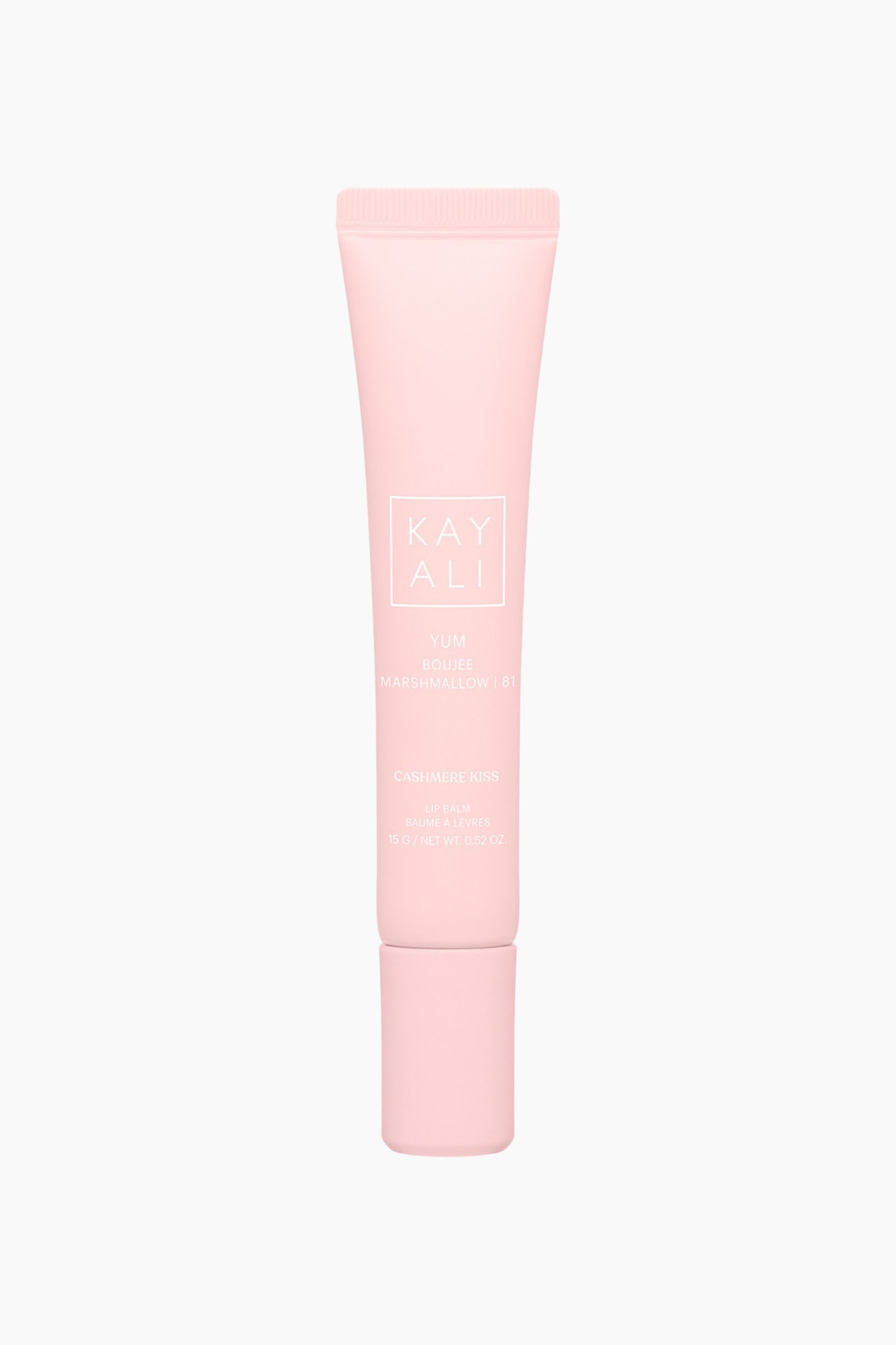 Visa större bild: Kayali Yum Boujee Marshmallow 81 Cashmere Kiss Lip Balm står upprätt och visar en pastellrosa kläm-tub med ett matchande cylindriskt lock längst ner. Framsidan av den matt yta tuben visar vit text, inklusive varumärkesnamnet "KAYALI" inuti en fyrkantig ram samt produktinformationen.