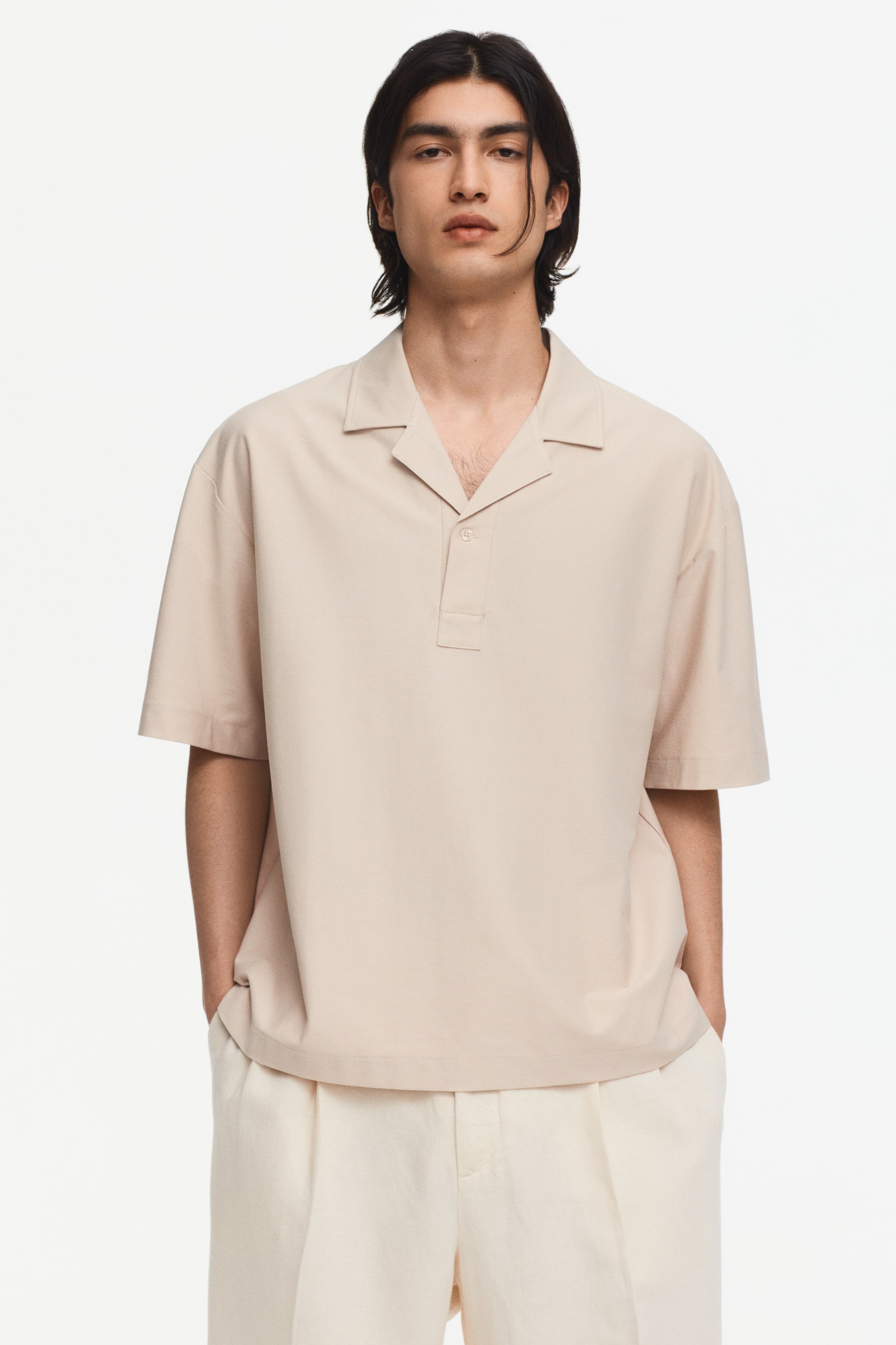 View larger image: A beige short-sleeve polo shirt is shown facing forward, featuring a spread collar, a one-button half-placket, and a relaxed fit with a straight hem.