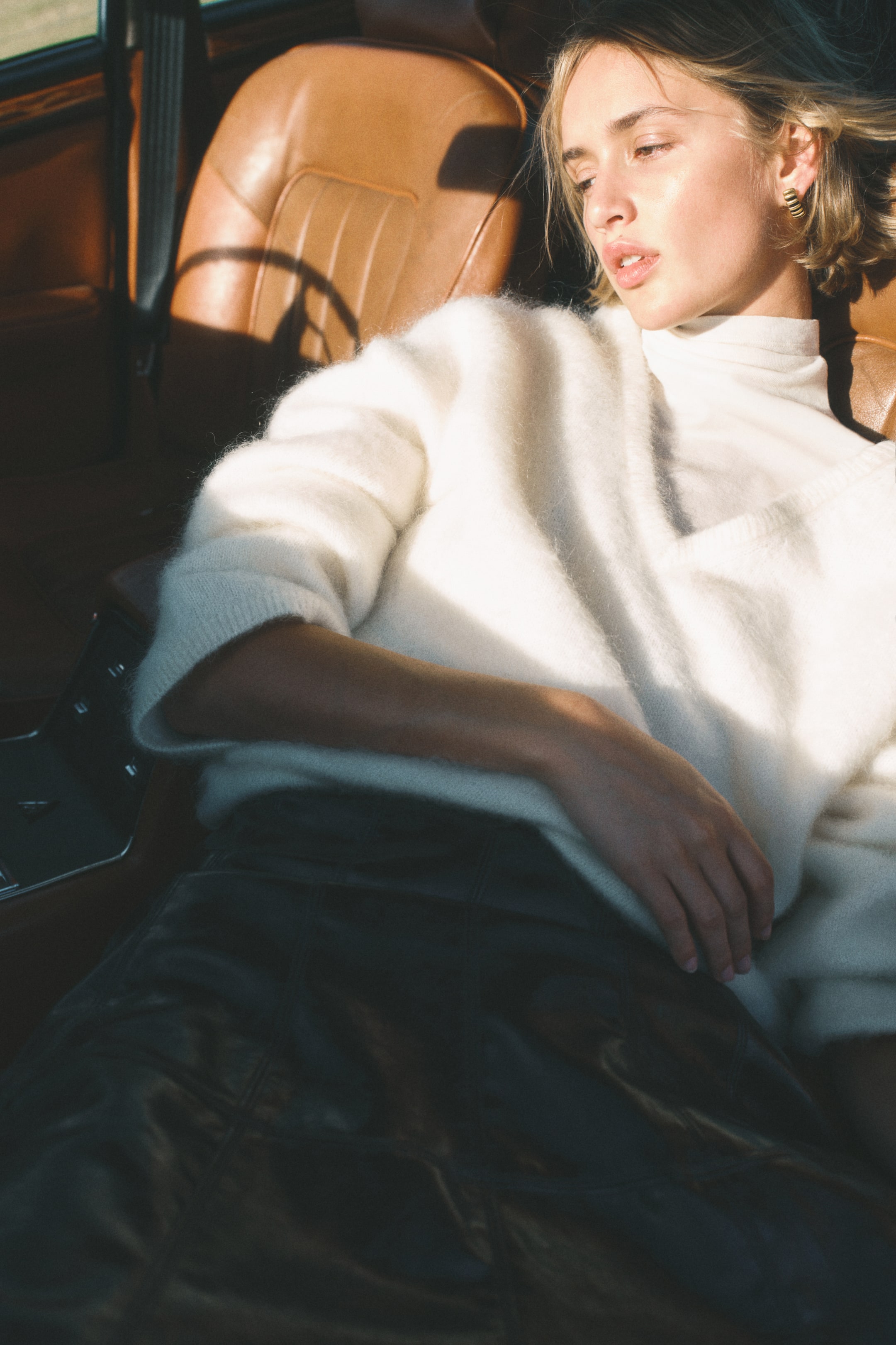 Grösseres Bild ansehen: Ein weißer, flauschiger Rollkragenpullover wird aus einer frontalen Perspektive präsentiert, mit entspannter Passform und gerippten Bündchen. Er wird über einem dunklen, glänzenden Rock mit sichtbaren Panelnähten getragen.