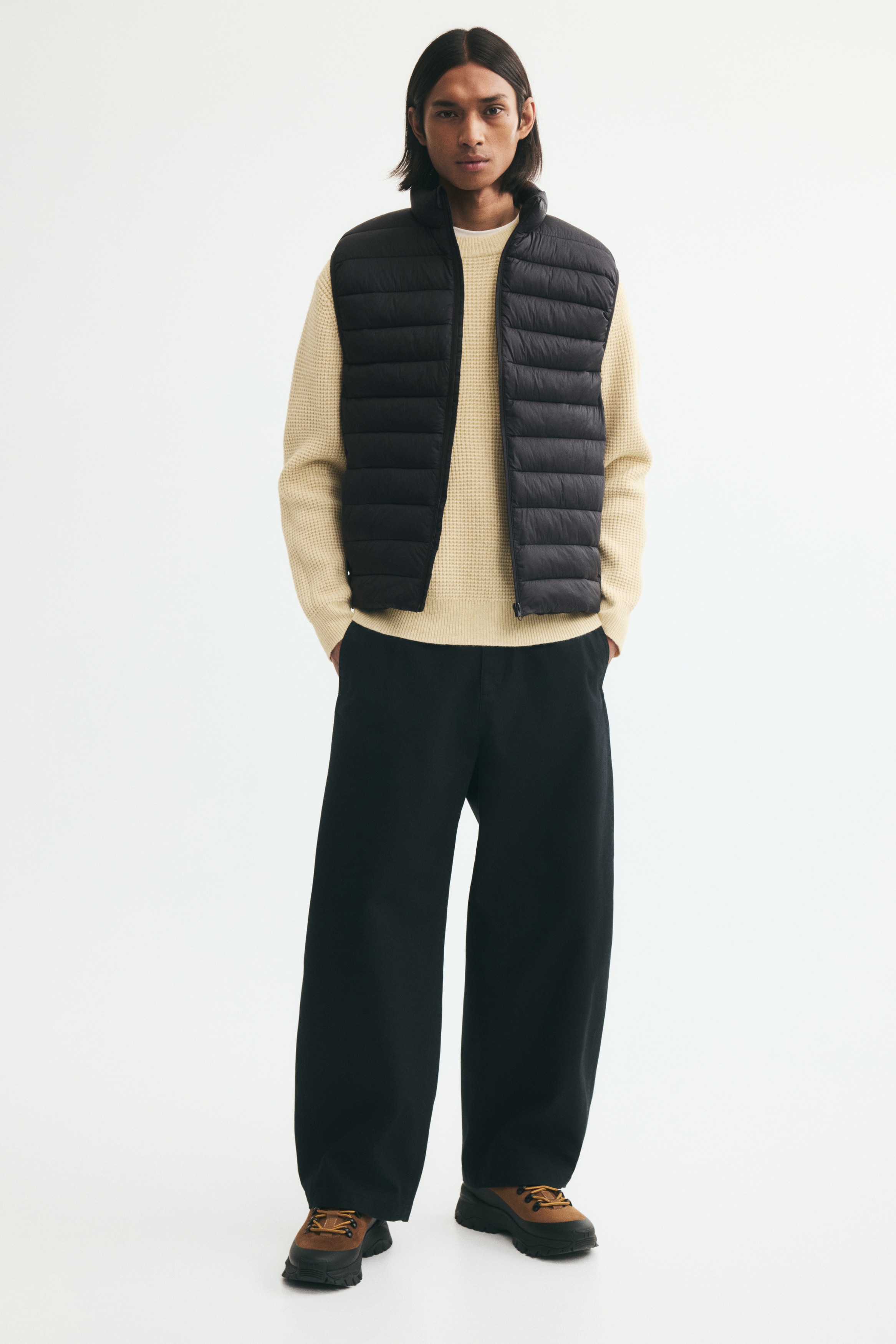 A black puffer vest is displayed from the front, featuring horizontal quilting throughout. It is designed with a stand-up collar and a full-zip front closure.