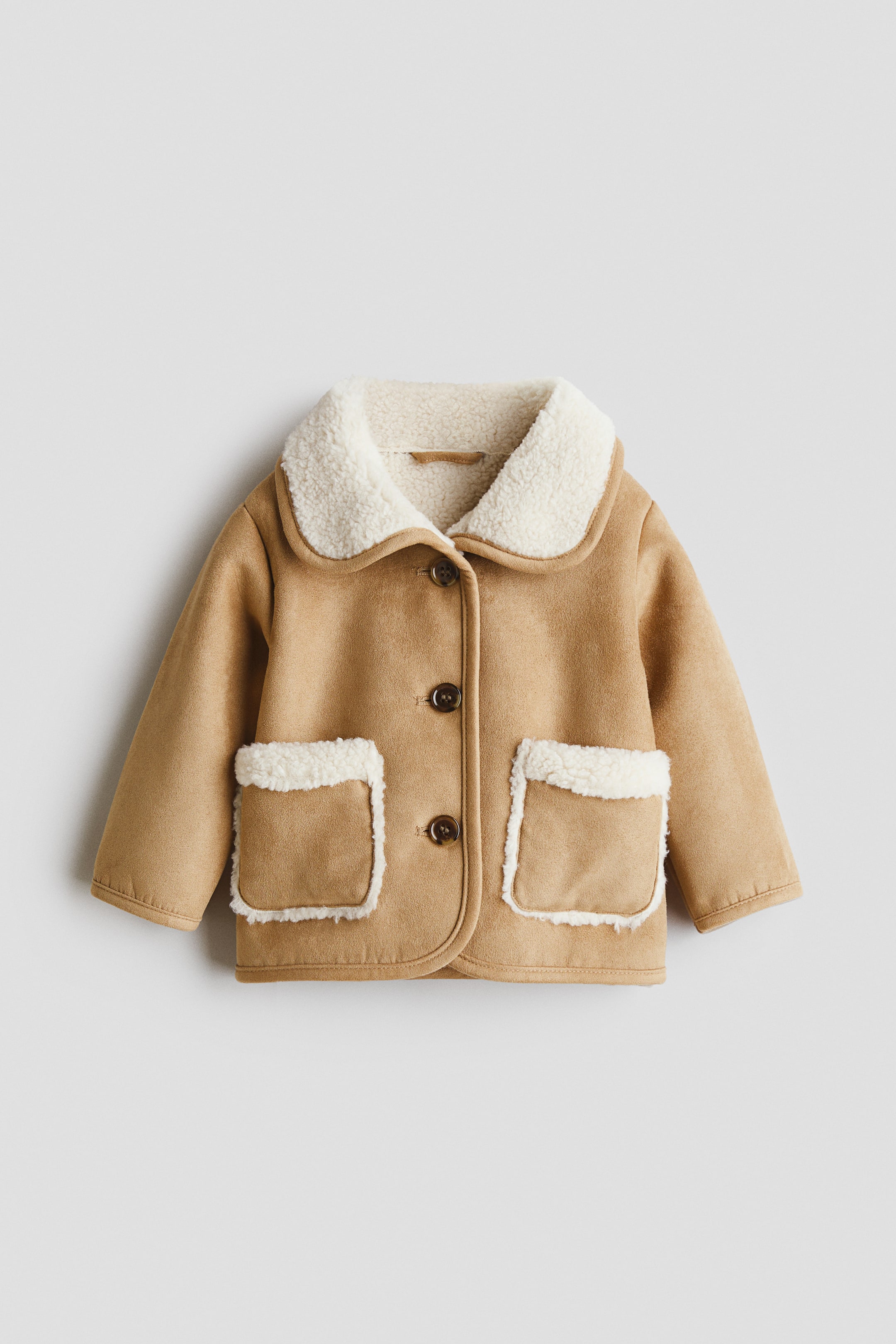 View larger image: A tan faux suede jacket is shown from the front, featuring a cream faux shearling collar and matching trim on two front patch pockets. Three dark brown buttons secure the front closure.