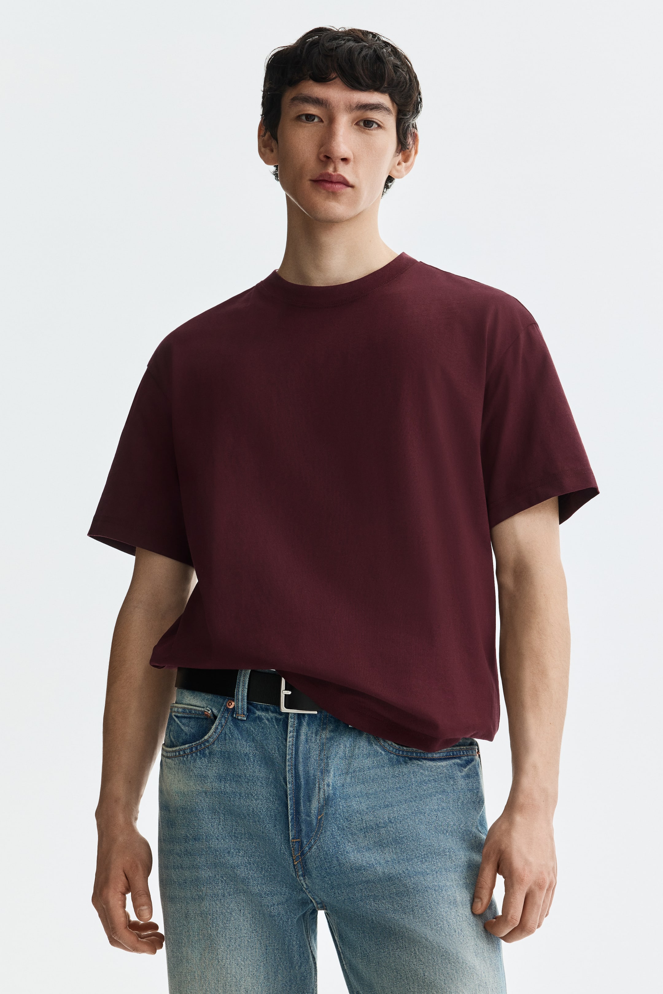 View larger image: A maroon t-shirt showcasing a ribbed crew neck and short, relaxed sleeves. It offers a loose fit, partially tucked into light wash jeans.