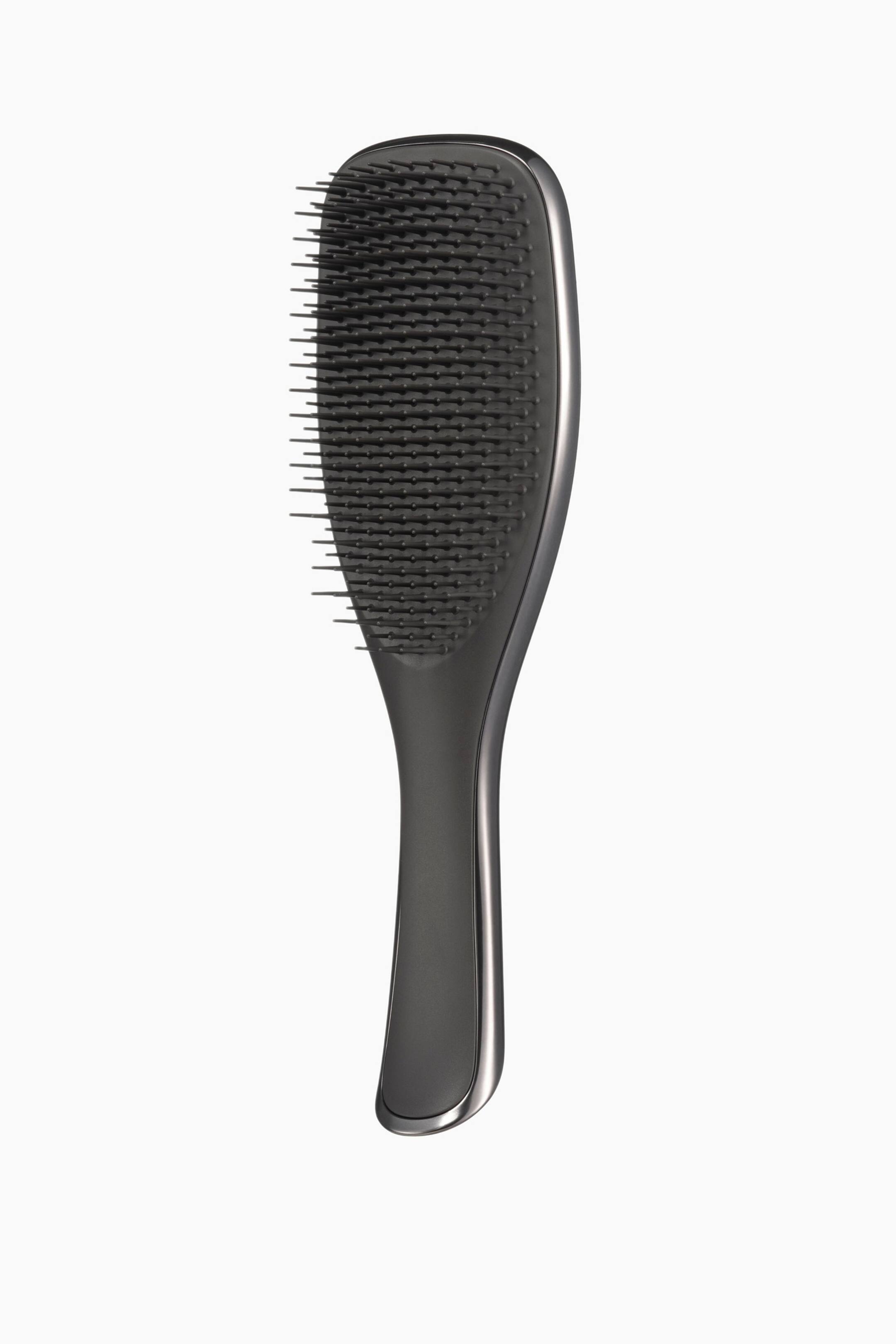 Visa större bild: En mörkgrå hårborste står upprätt, något vinklad åt höger. Borsten har ett konturerat handtag med en blank list och ett ovalt huvud inbäddat med många korta, mörka borststrån i varierande längder.