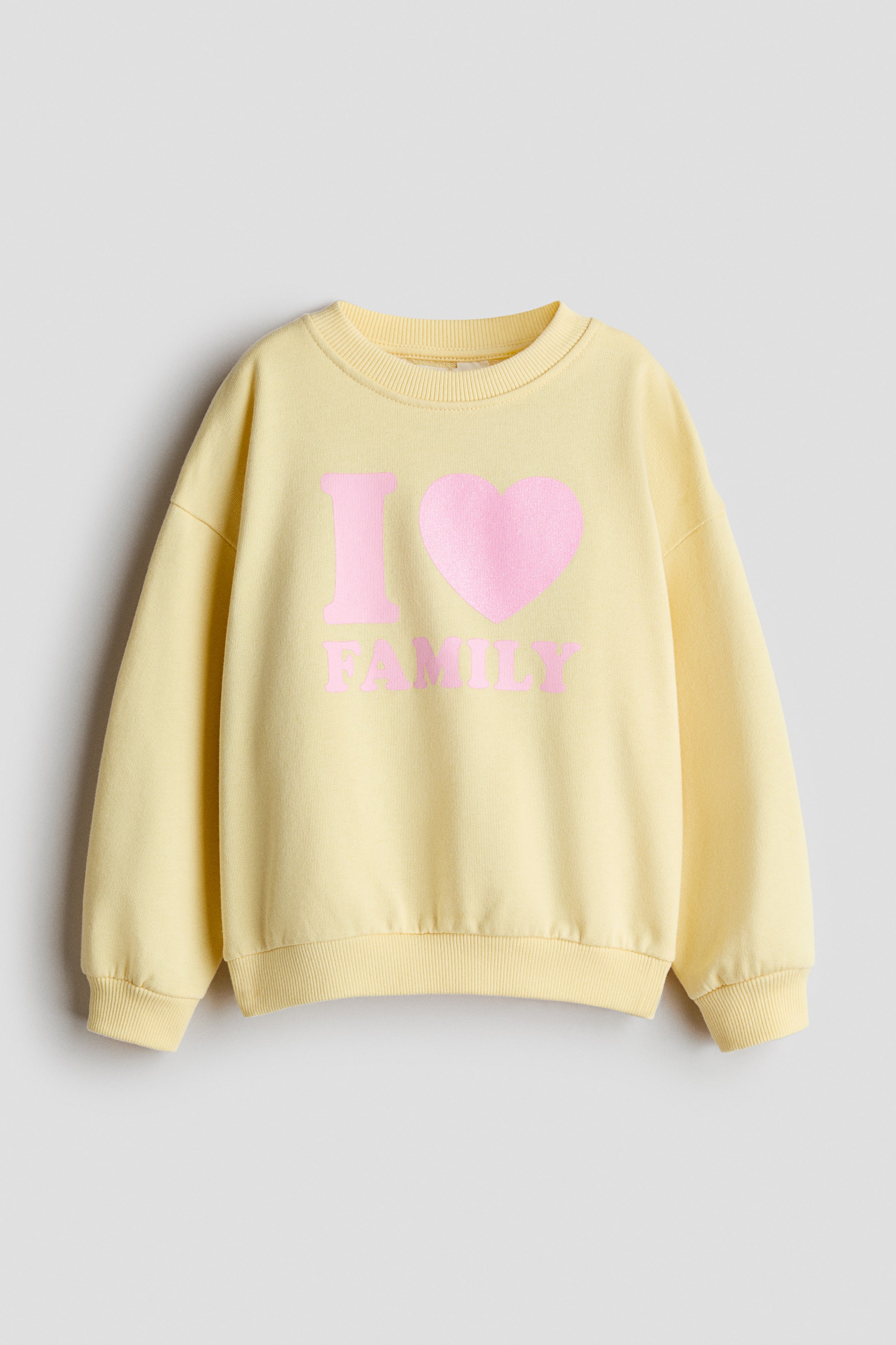 View larger image: A light yellow sweatshirt is shown from the front, featuring a round, ribbed neckline, dropped shoulders, and ribbed cuffs and hem. The front displays a pink graphic design reading "I", followed by a heart symbol, and "FAMILY" underneath.