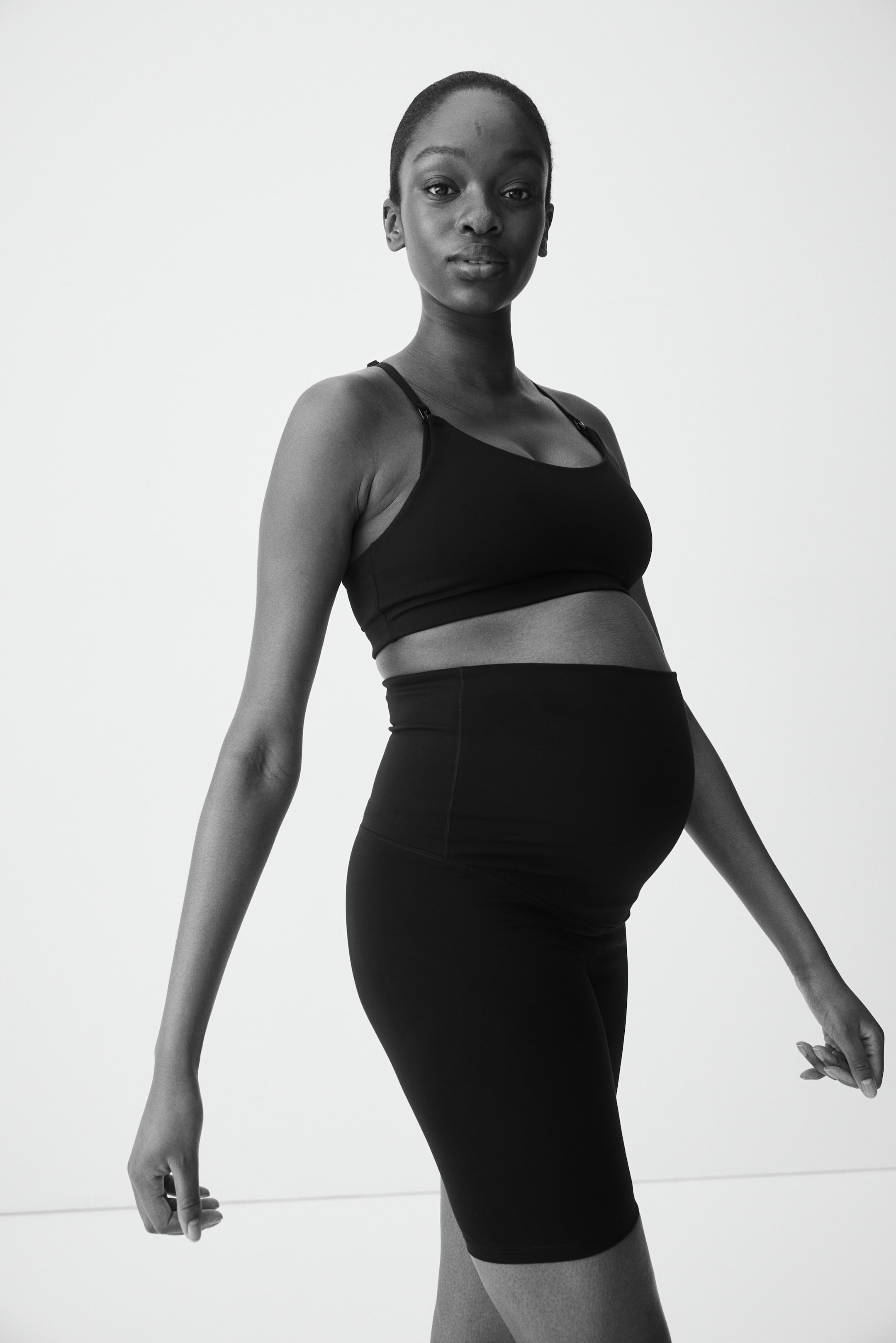 Se større billede: Et sort sæt graviditets træningstøj omfatter en sports-bh med rund hals, tynde justerbare stropper og højtaljede cykelshorts. Shortsene har et bredt, støttende panel, der dækker maven og strækker sig til midt på låret.