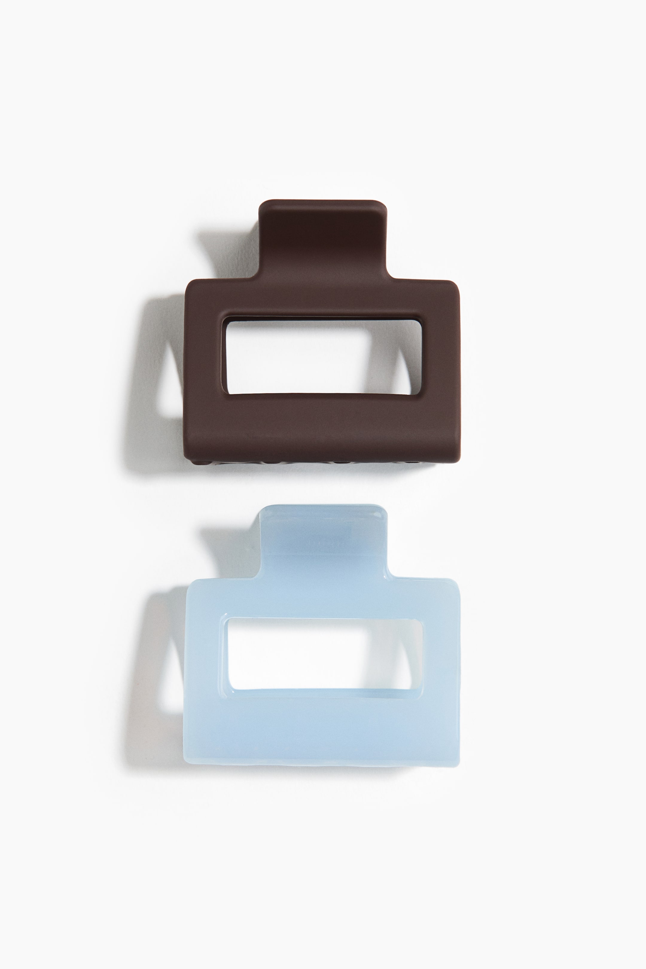 Zobacz większy obraz: Dwie prostokątne, plastikowe klamry do włosów, każda o długości 5 cm, pokazane z przodu (FRONT): jedna ciemnobrązowa, druga przezroczysta, jasnoniebieska; obie mają prostokątny korpus z centralnym wycięciem.