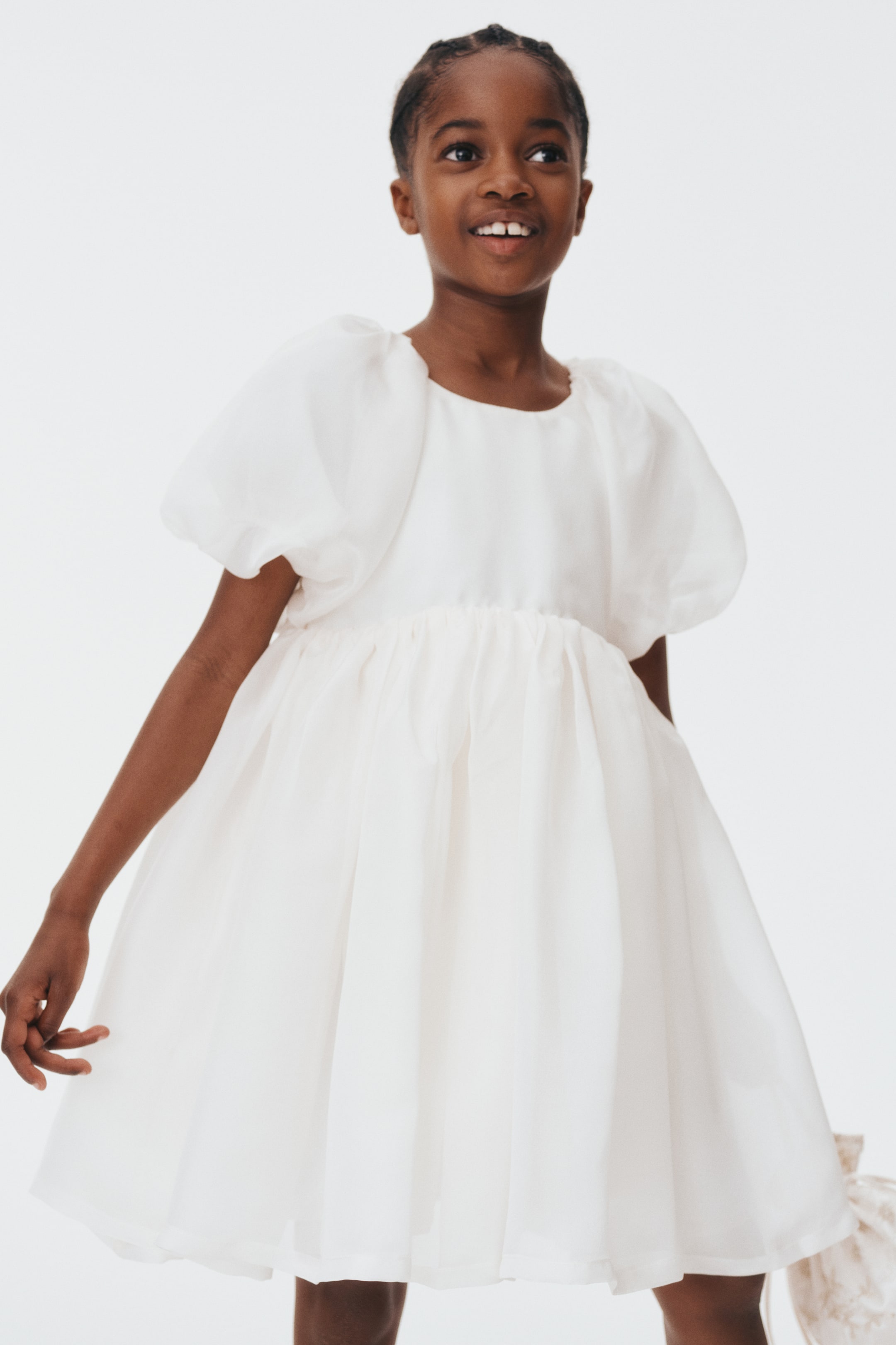 הצגת תמונה גדולה יותר: השמלה הלבנה מתאפיינת בצווארון עגול ובשרוולים קצרים ונפוחים. מותן מכווצת מובילה לחצאית מלאה וזורמת שנופלת מעל הברכיים.