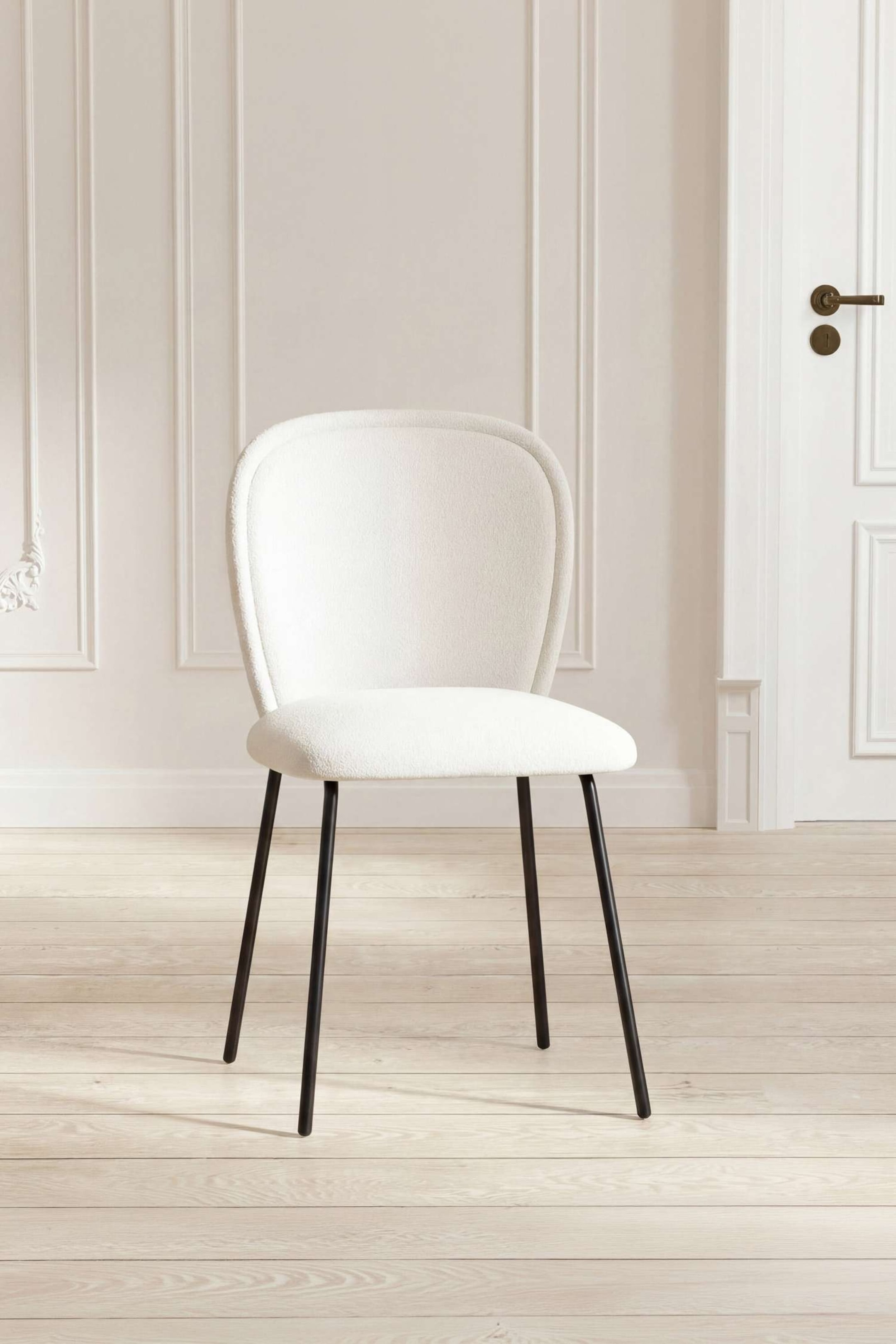 Agrandir l'image: Une chaise est légèrement inclinée vers la droite, avec un dossier arrondi et incurvé et un siège rembourré recouvert d'un tissu blanc texturé. Elle repose sur quatre pieds élancés en métal sombre qui s'évasent légèrement vers l'extérieur.