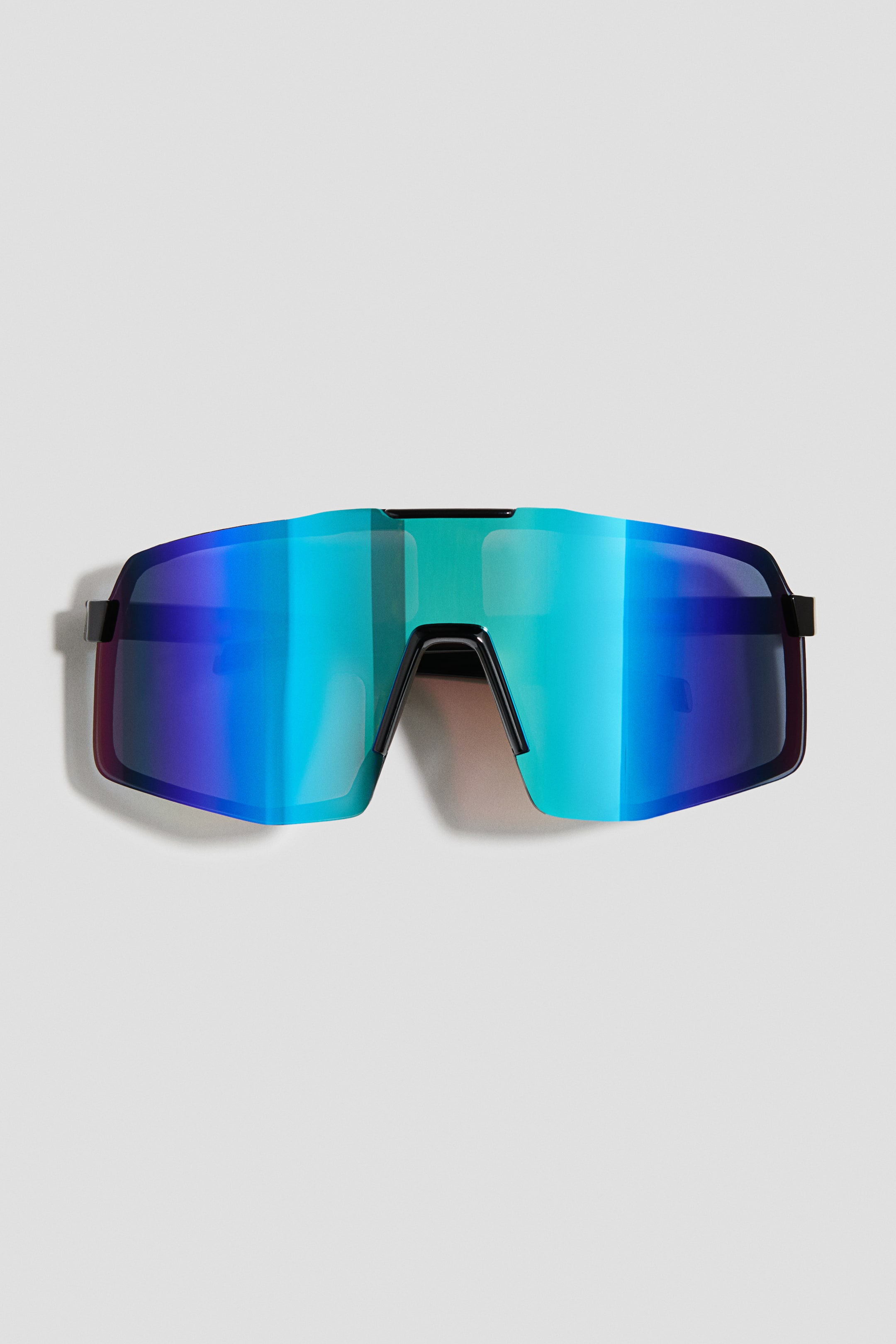 View larger image: Sunglasses facing front feature a single-piece, oversized shield lens with a vibrant blue, green, and purple mirrored gradient. The sunglasses display a black frame structure at the bridge and temples.