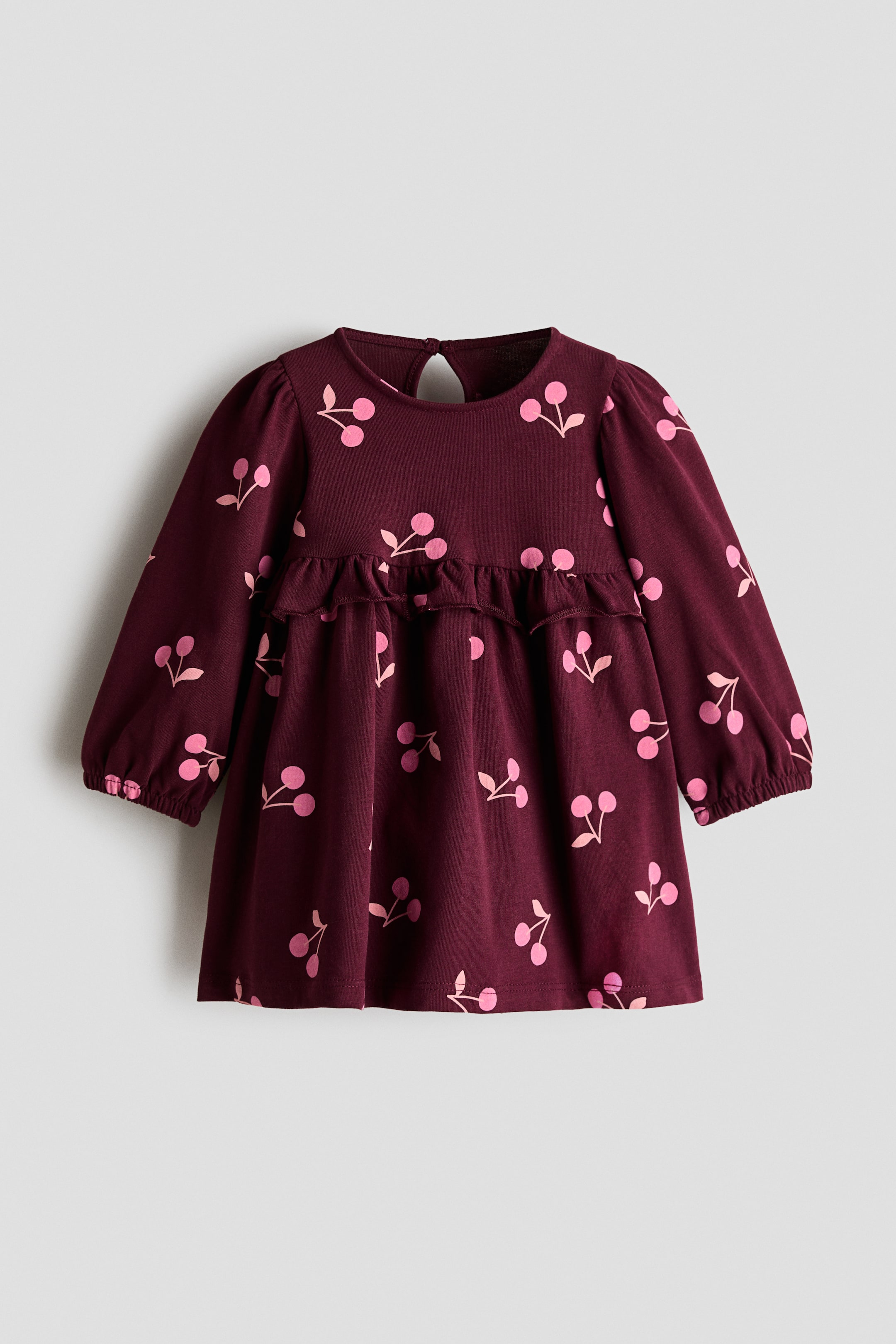 View larger image: A front-facing dress showcases a burgundy fabric adorned with an all-over pink cherry print. It features a round neckline with a keyhole opening at the back, long puffed sleeves with elasticated cuffs, and a horizontal ruffle detailing the waistline, separating the bodice from a gathered skirt.