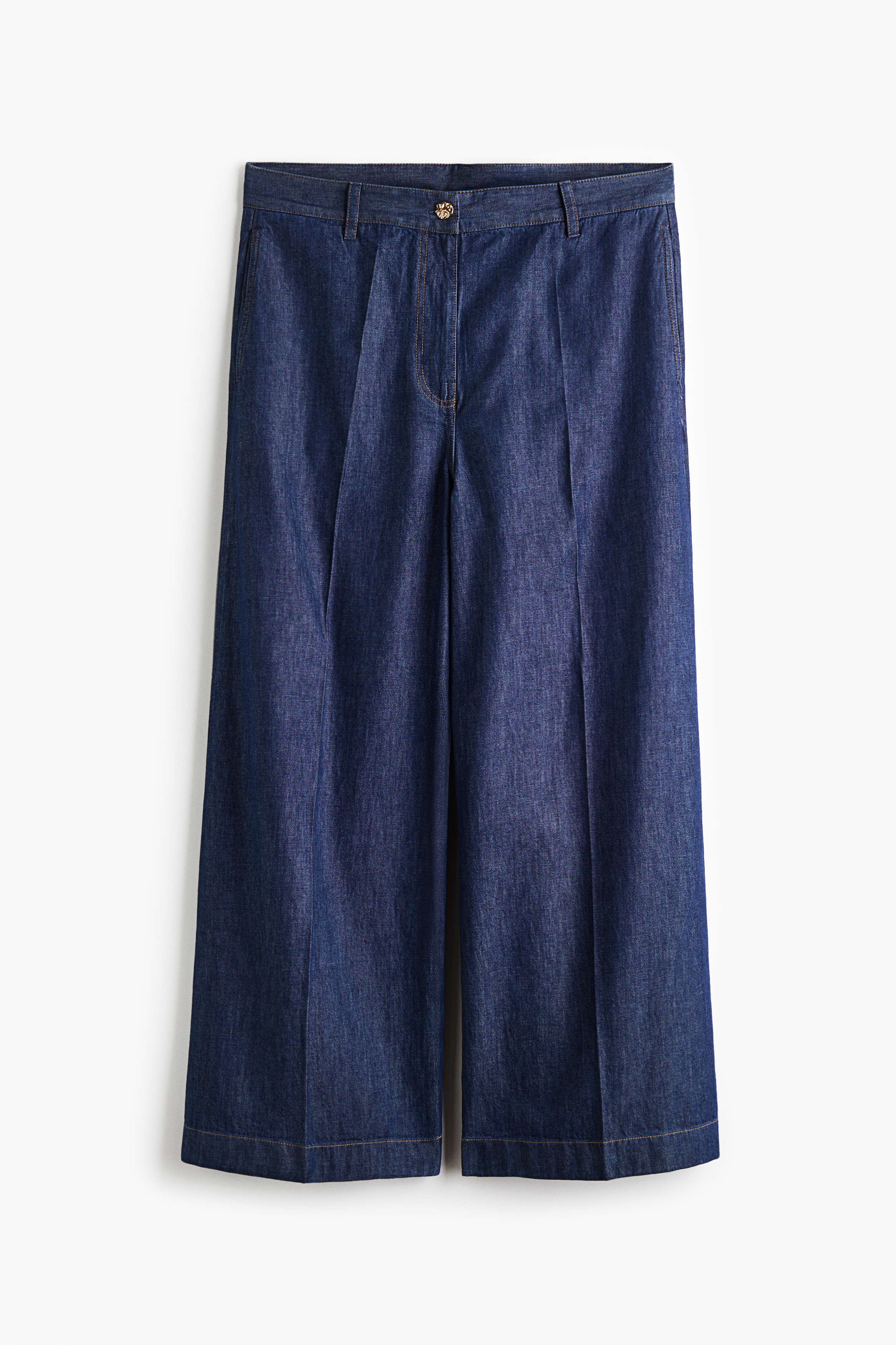 A pair of dark wash denim wide-leg trousers is shown from the front, featuring a high-rise waist with belt loops, a gold-tone button closure, and a zip fly. Sharp pressed creases run down the centre of each wide leg, finished with contrasting topstitching along the hem.