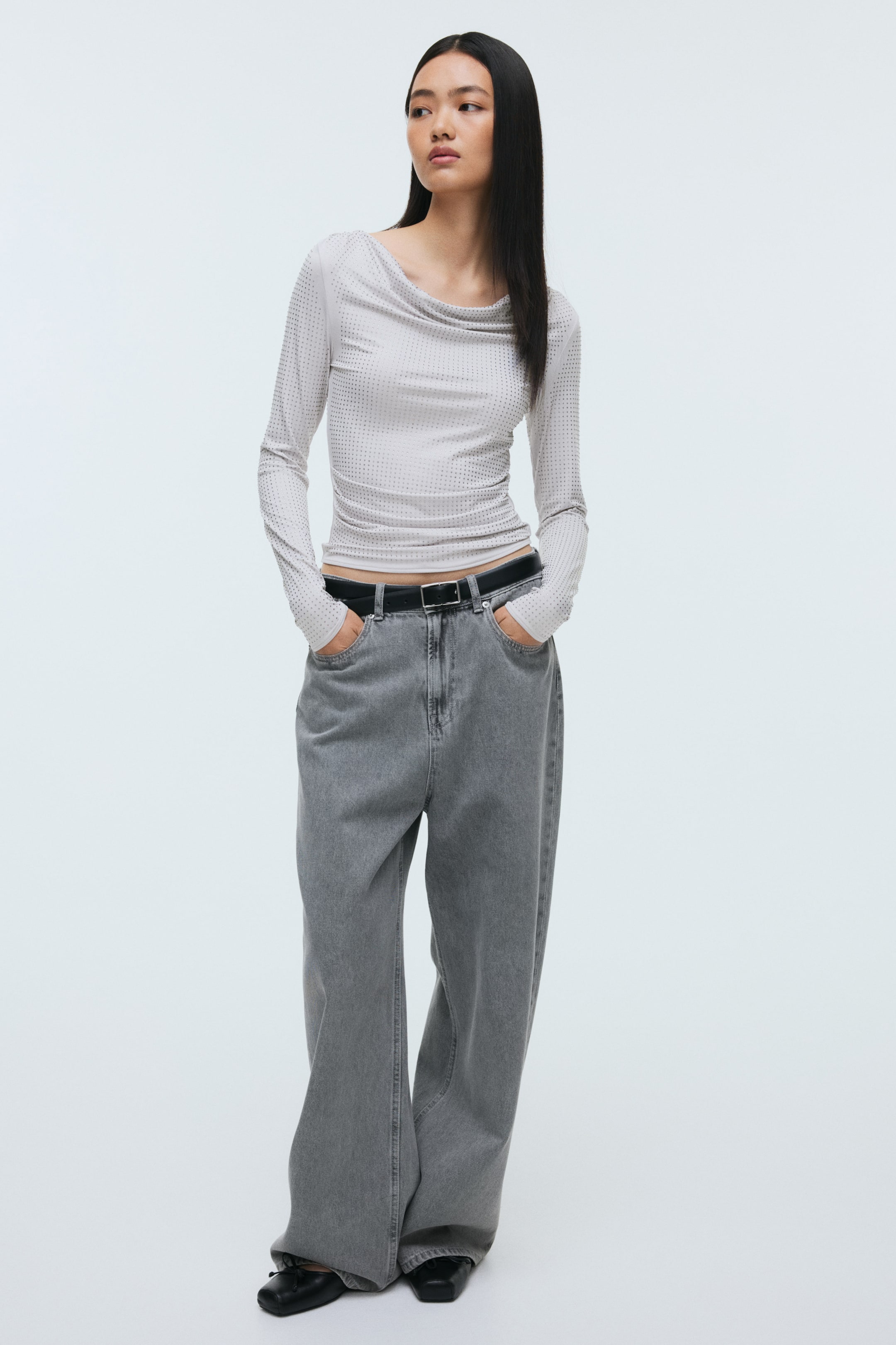 Grösseres Bild ansehen: Ein hellgraues Langarmoberteil wird aus einer Frontalansicht präsentiert, mit einem drapierten Wasserfallausschnitt. Es zeigt ein allover-Muster aus kleinen, dunklen Punkten und liegt eng am Körper an.