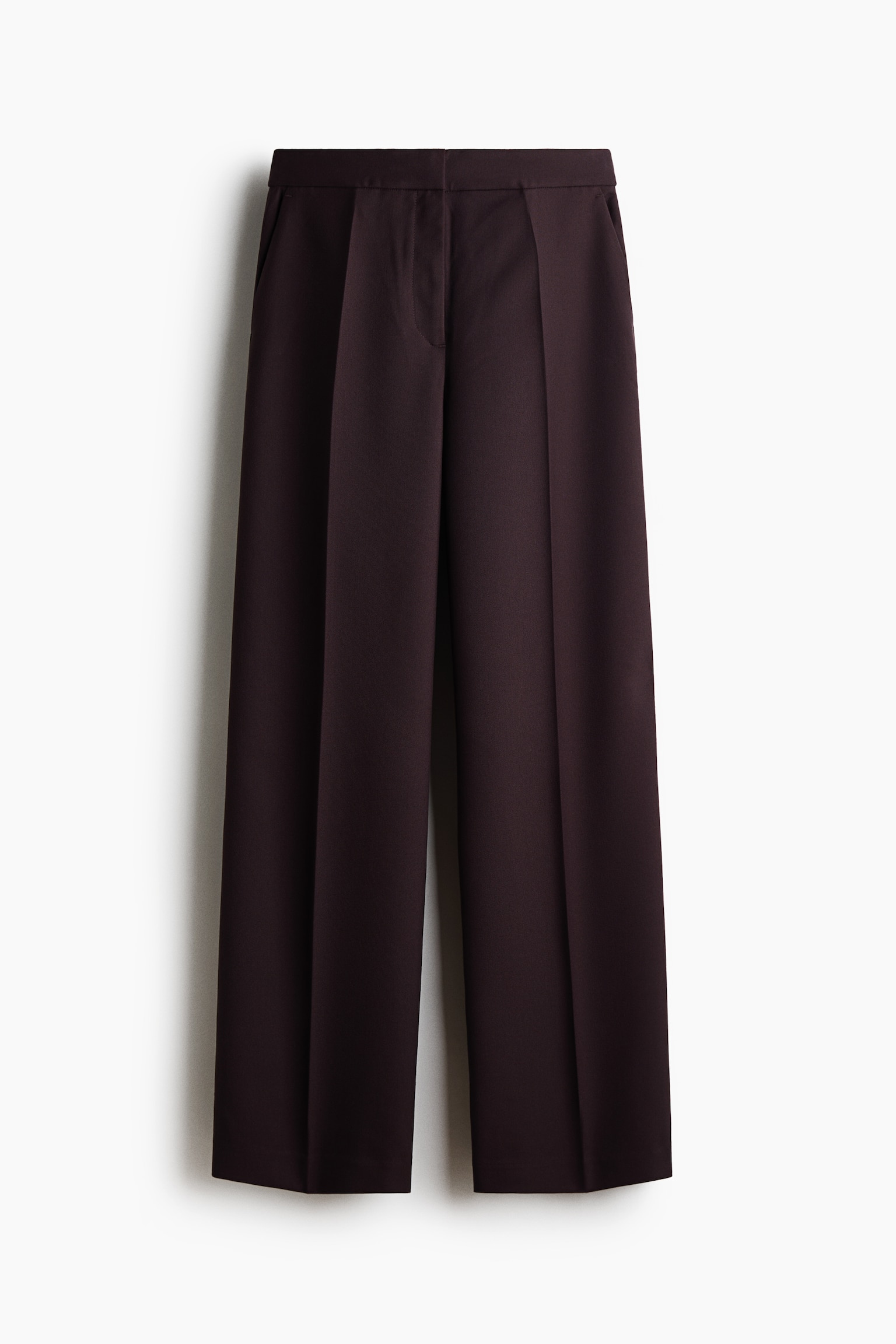 Dark plum pants in a textured weave are shown from the front, featuring a straight-leg silhouette with sharp pressed creases running down the center of each leg. The design includes a flat waistband with a concealed zip fly and subtle diagonal side pockets.