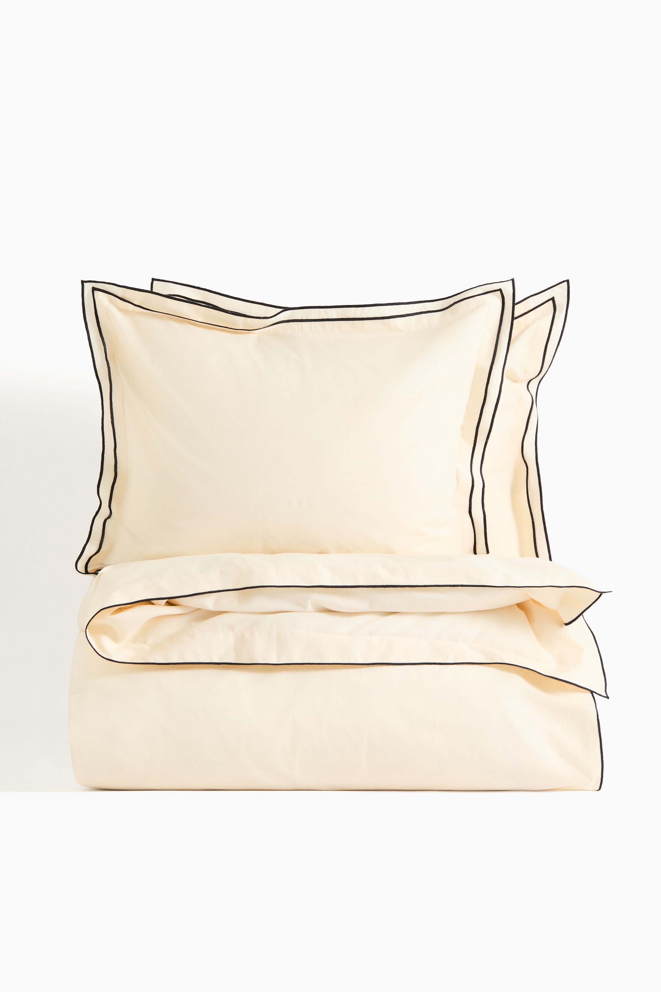 View larger image: A double/king duvet cover set is presented front-on, showcasing cream-coloured fabric with black trim. Two pillowcases are positioned at the top, each featuring a double-winged border, while the duvet cover is folded beneath, revealing a single-wing border along its top edge.