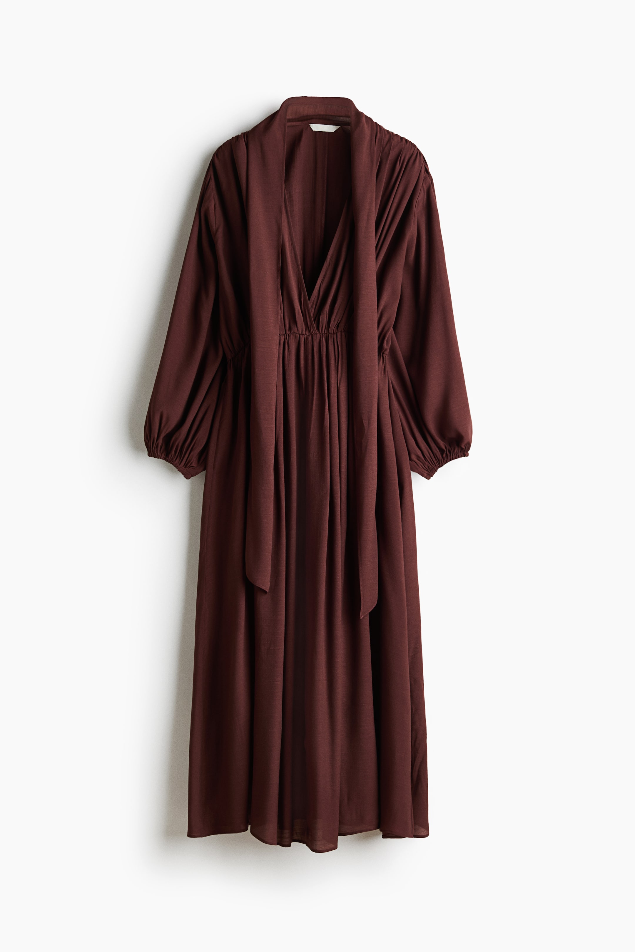 View larger image: The calf-length dress is showcased from the front, displaying a draped effect created by gathered fabric throughout its design. It features a deep V-neckline with a subtle overlap, a sewn-in scarf, long balloon sleeves with elasticated cuffs, a gathered waistline, and a gently flared skirt.