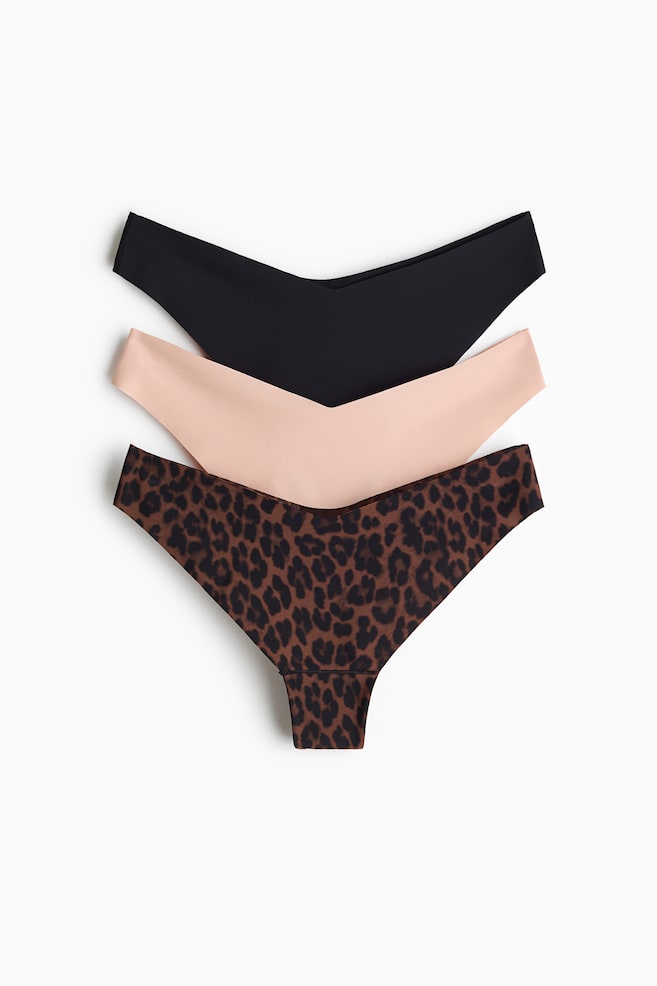 Drei Paar nahtlose Damen-Strings werden in einer vertikalen Stapelung von vorne prÃ¤sentiert. Das Set umfasst oben ein einfarbig schwarzes Paar, in der Mitte ein einfarbig hellpfirsichfarbenes Paar und unten ein braun gemustertes Paar im Leopardenprint, alle mit einem tief ausgeschnittenen, V-fÃ¶rmigen Bund gestaltet. - 1
