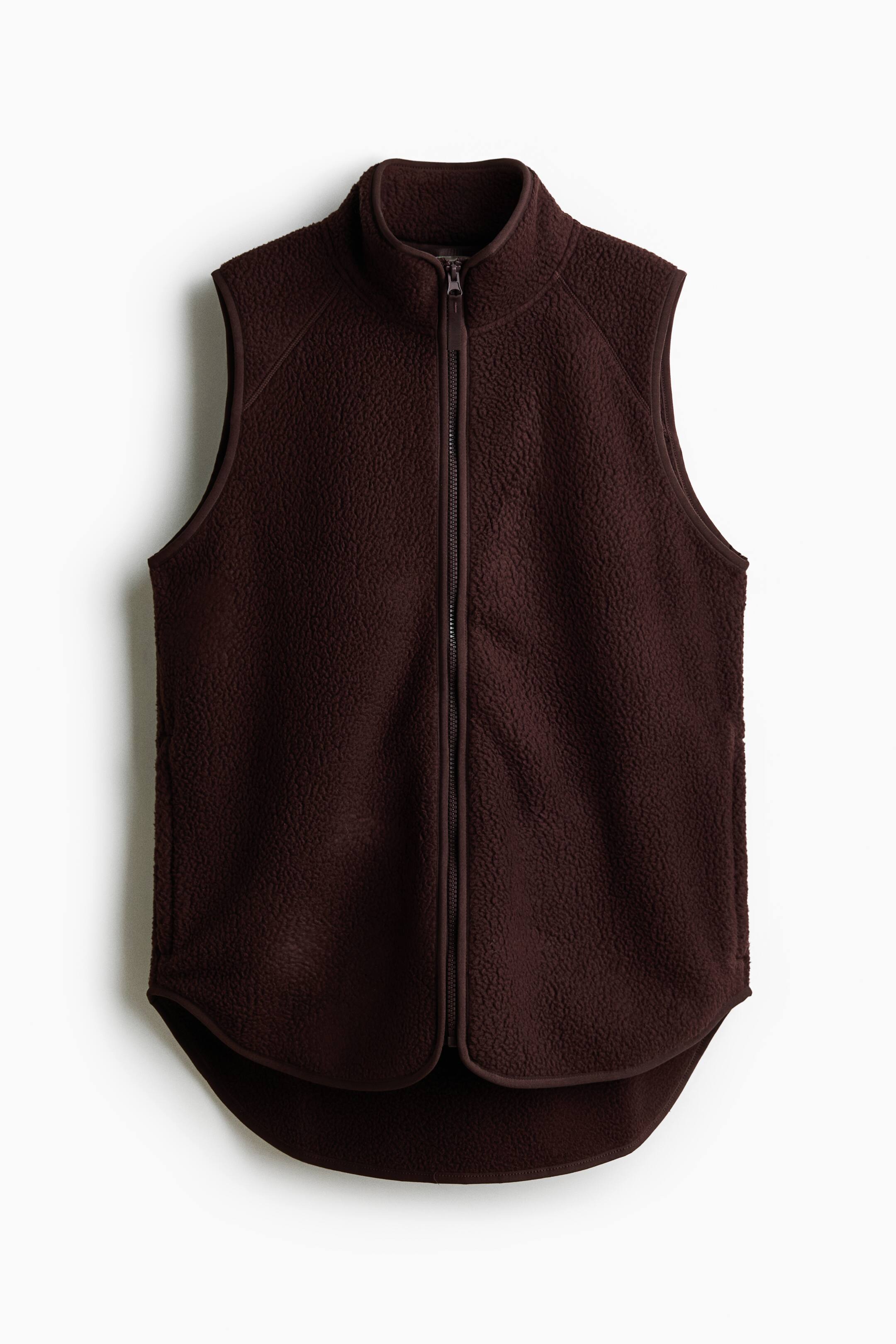 Grotere afbeelding bekijken: Een donkerbruine teddyfleece sportgilet wordt van voren getoond, met een hoge kraag, een volledige ritssluiting en zijzakken met rits. Het is afgewerkt met elastische boorden langs de randen en een afgeronde zoom.