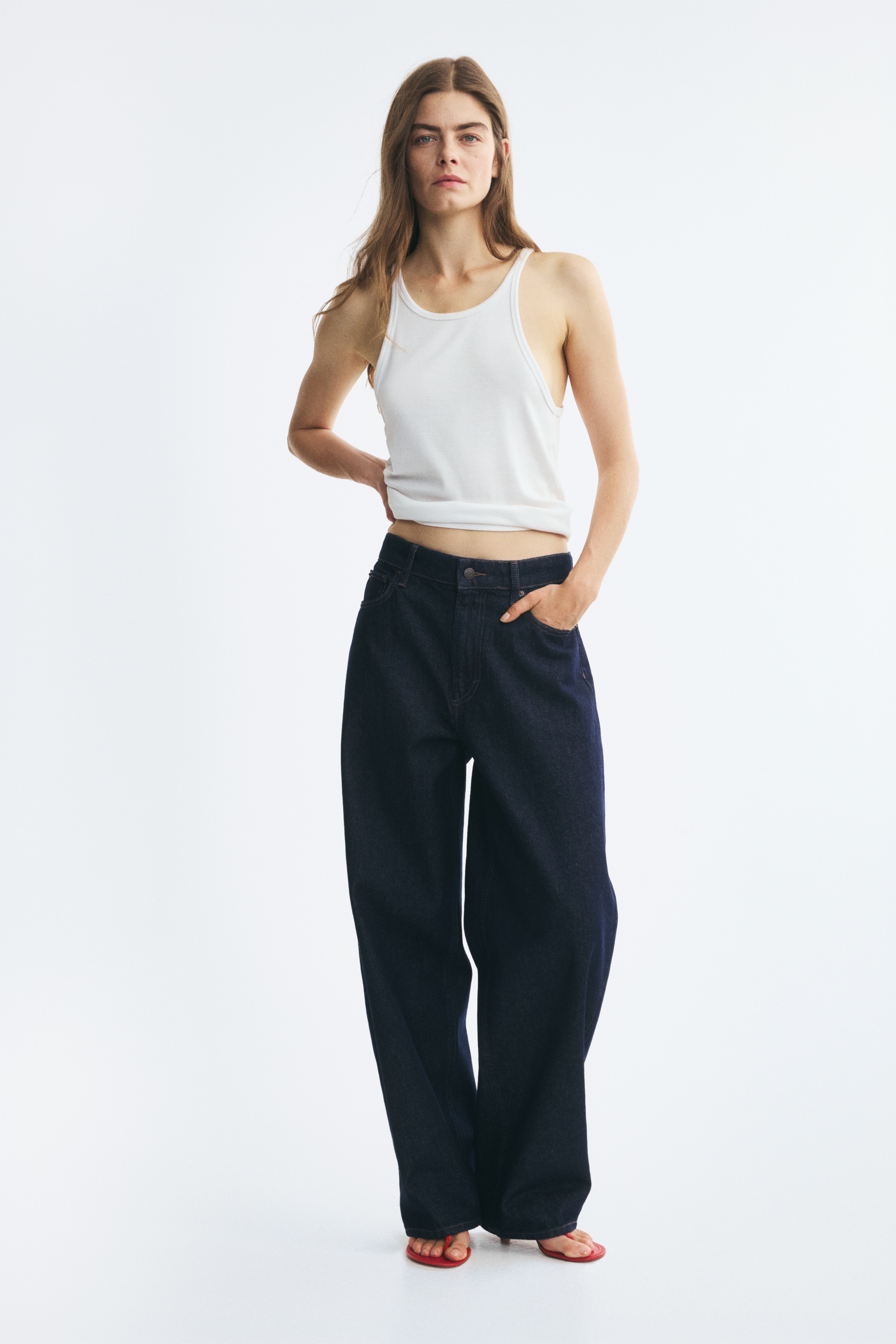 Má»t chiếc quần jeans denim xanh navy Äáºm, thiết kế 5 túi, ÄÆ°á»£c chụp từ phÃa trưá»c, ná»i báºt vá»i cạp lá»ng dáng regular-rise, khóa cà i nút, khóa kéo và các Äai thắt lưng. Quần có phom á»ng rá»ng, cấu trúc rõ nét, hÆ¡i thuôn nhẹ vá» phÃa gấu, ÄÆ°á»£c nhấn bằng ÄÆ°á»ng chá» may mà u cam tương phản.