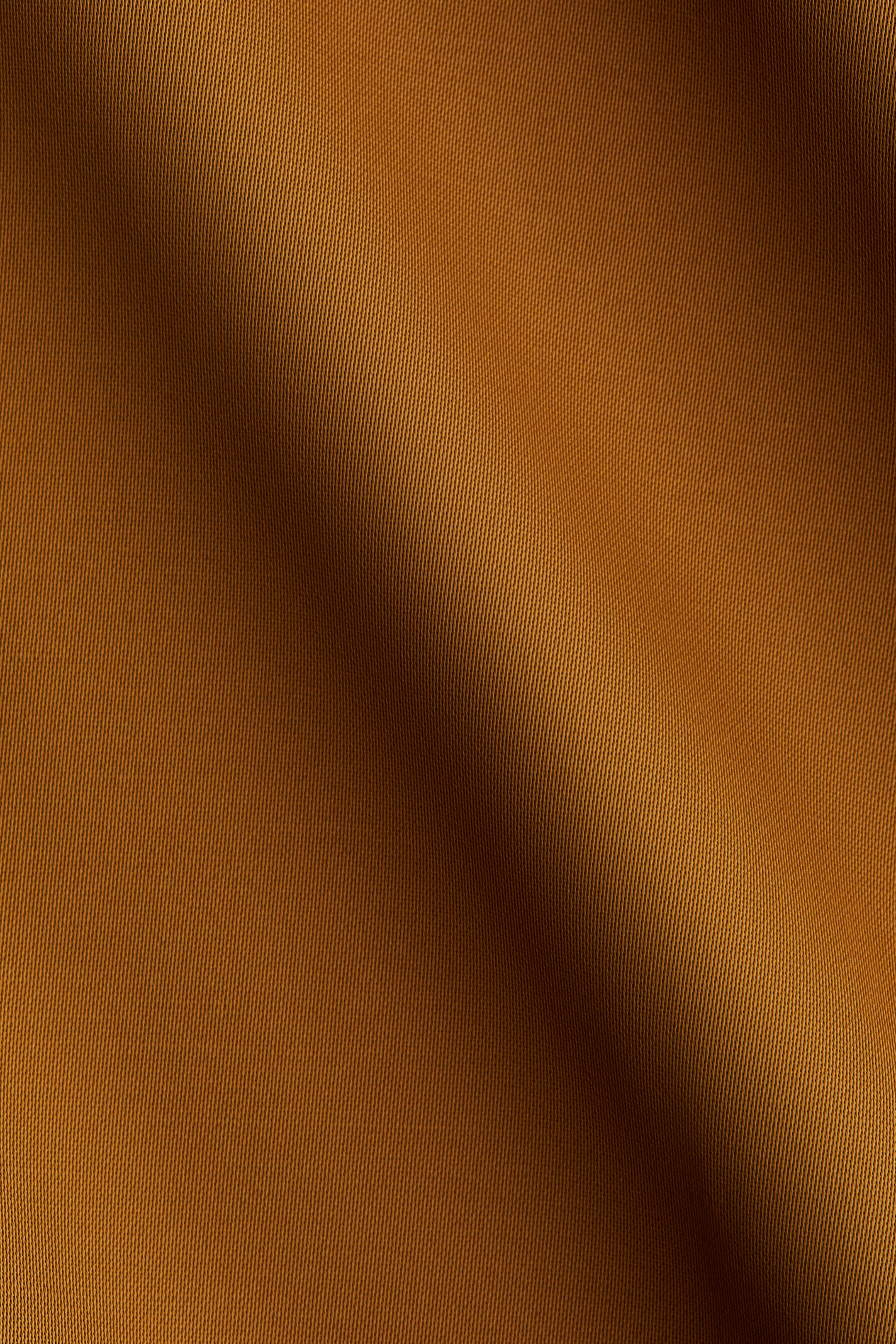 Ver imagen más grande: Una tela de color rojizo presenta un patrón de tejido en sarga diagonal. Se drapea suavemente, creando pliegues y sombras suaves a lo largo de su superficie.