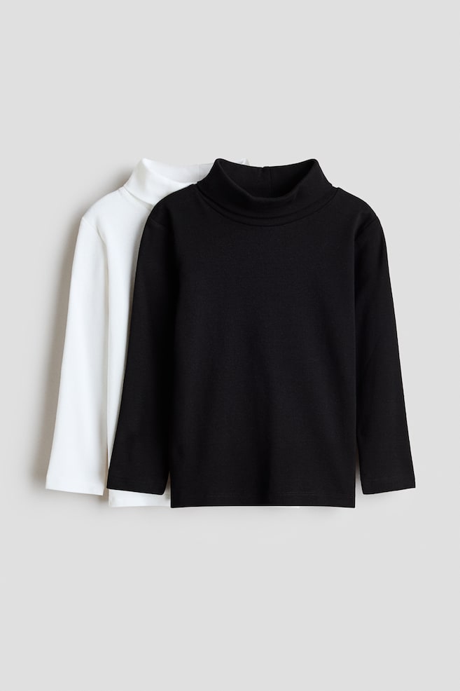 A pair of long-sleeve mock-neck tops is shown from the front, featuring a solid black top layered directly in front of a solid white top. Both garments are displaying a clean, minimalist design with long sleeves and high, folded necklines. - 1