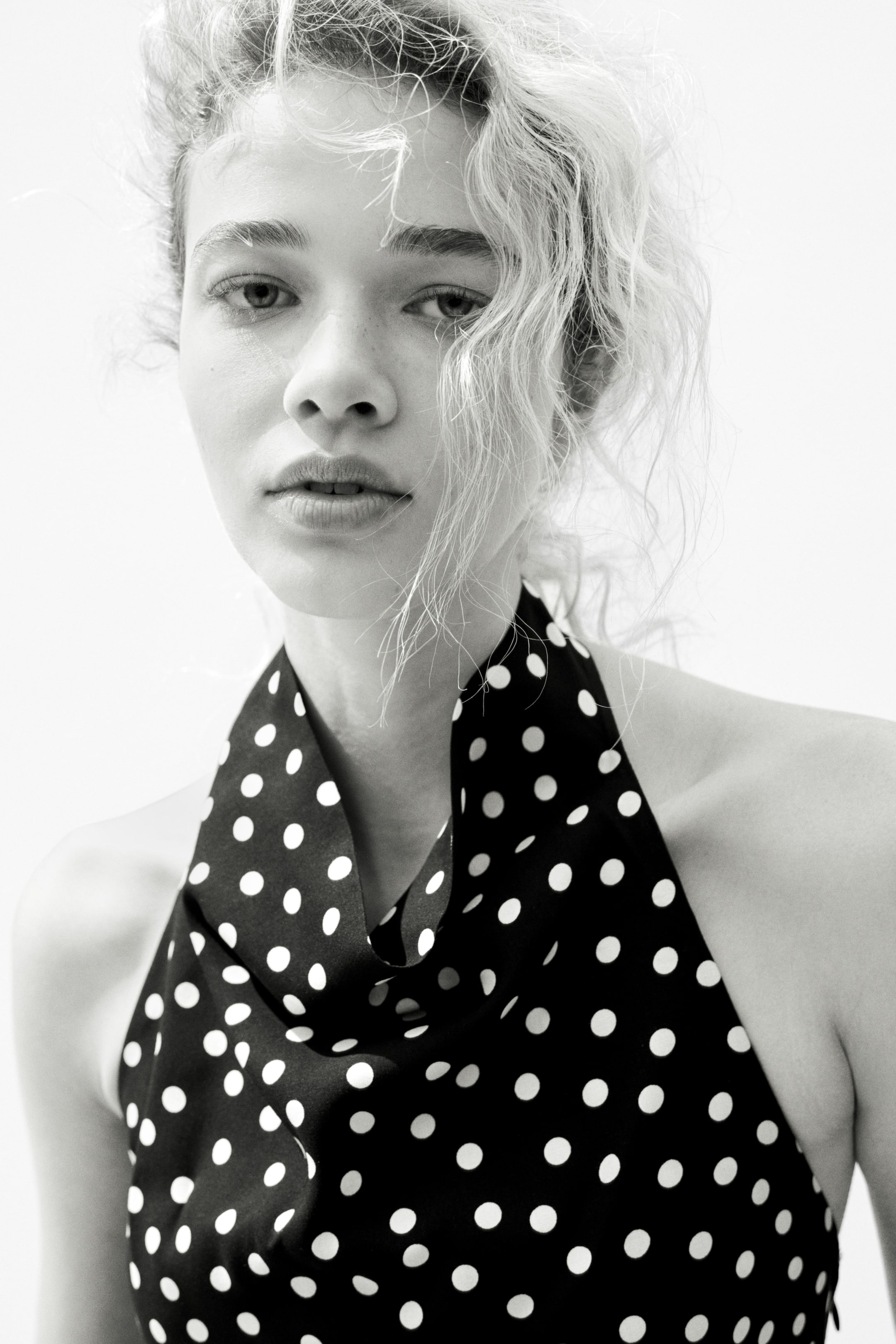 View larger image: "This black and white polka dot top boasts a draped cowl neckline. The black fabric is adorned with evenly spaced white polka dots, elegantly showcasing its soft drape across the chest."