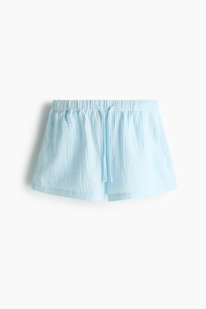 The light blue loose-fit shorts are showcasing an airy cotton muslin fabric, featuring an elasticated, drawstring waist and discreet side pockets. - 1