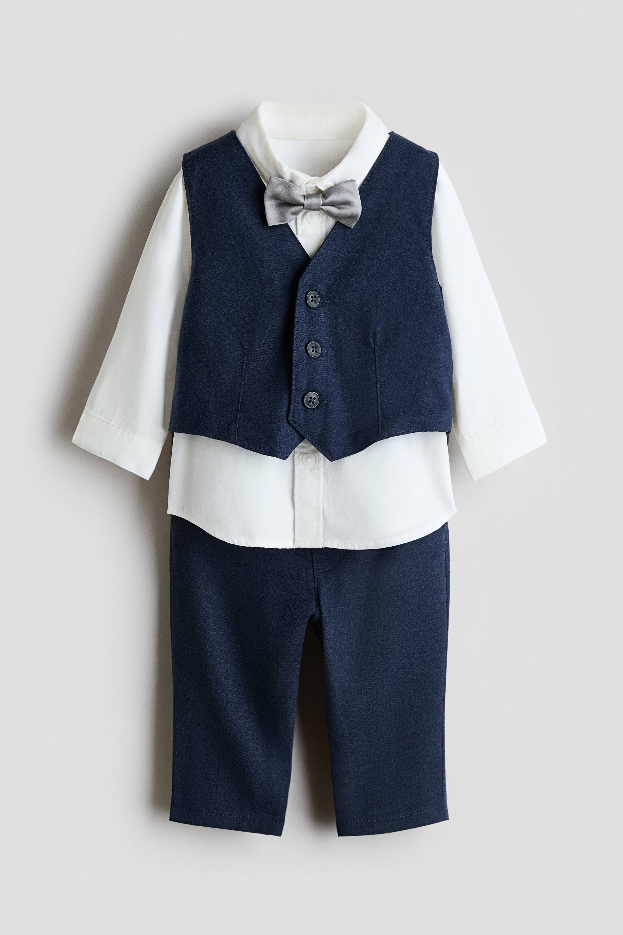 View larger image: A children’s dressy set is shown facing front, featuring a dark navy blue waistcoat layered over a white long-sleeve button-down shirt with a grey bow tie at the collar. The set is completed with matching dark navy blue pants.