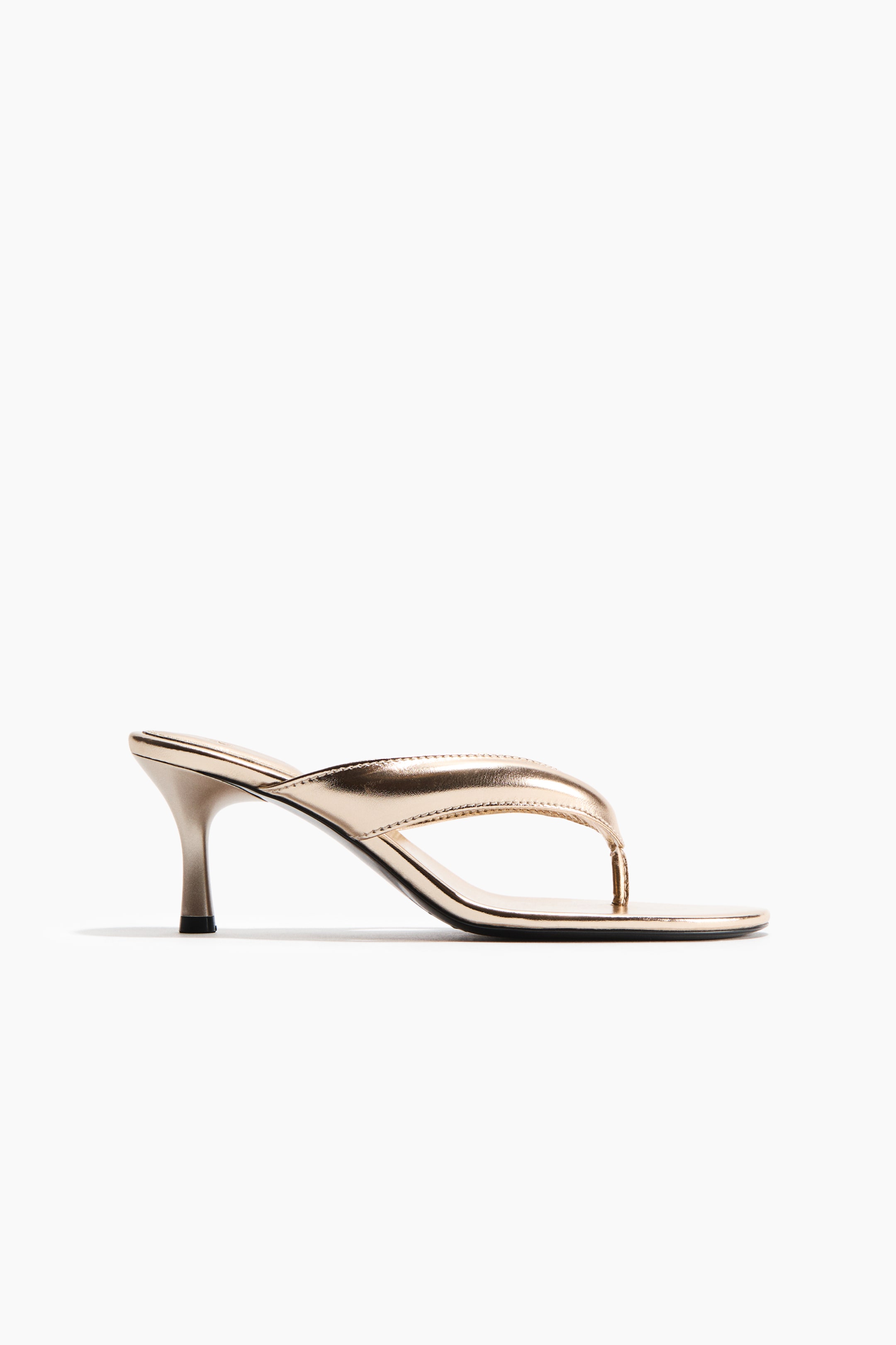 View larger image: Presenting a metallic gold mule-style sandal in its side profile, this piece showcases a sleek kitten heel, a square toe, and a thong strap.