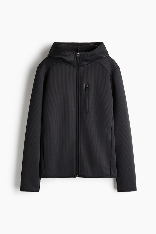 Ein schwarzer, strukturierter Hoodie mit ReiÃverschluss ist frontal ausgerichtet und verfügt über einen durchgehenden FrontreiÃverschluss sowie eine angesetzte Kapuze. Die Jacke zeigt auf der linken Seite eine vertikale Brusttasche mit ReiÃverschluss und getaptem Rand sowie ein feines, vertikal geripptes Stoffmuster im gesamten Design. - 1