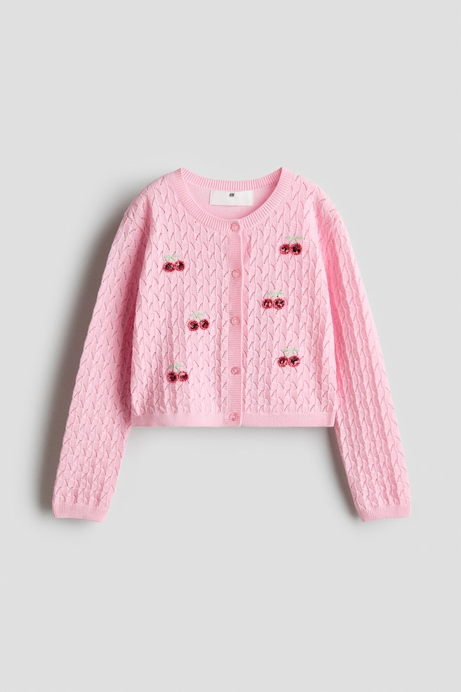 A pink cardigan is presenting its front, featuring a pointelle knit pattern throughout. It is adorned with several red sequin cherry appliqu�s and includes a crew neck, a front button placket with matching pink buttons, and ribbed cuffs and hem. - 1