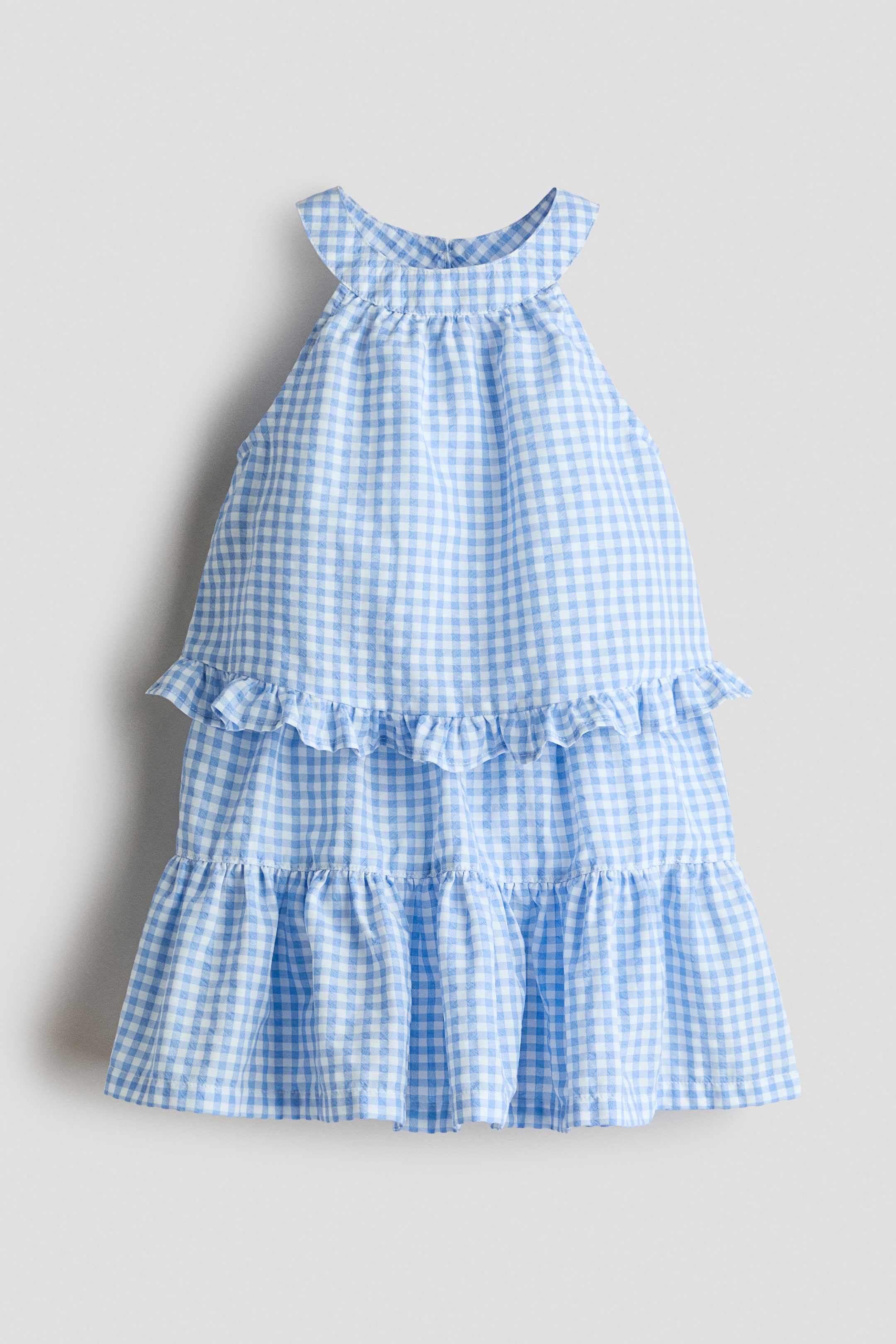 View larger image: A blue and white gingham check dress features a halter neckline with straps crossing at the back, complemented by a tiered skirt with ruffled layers.