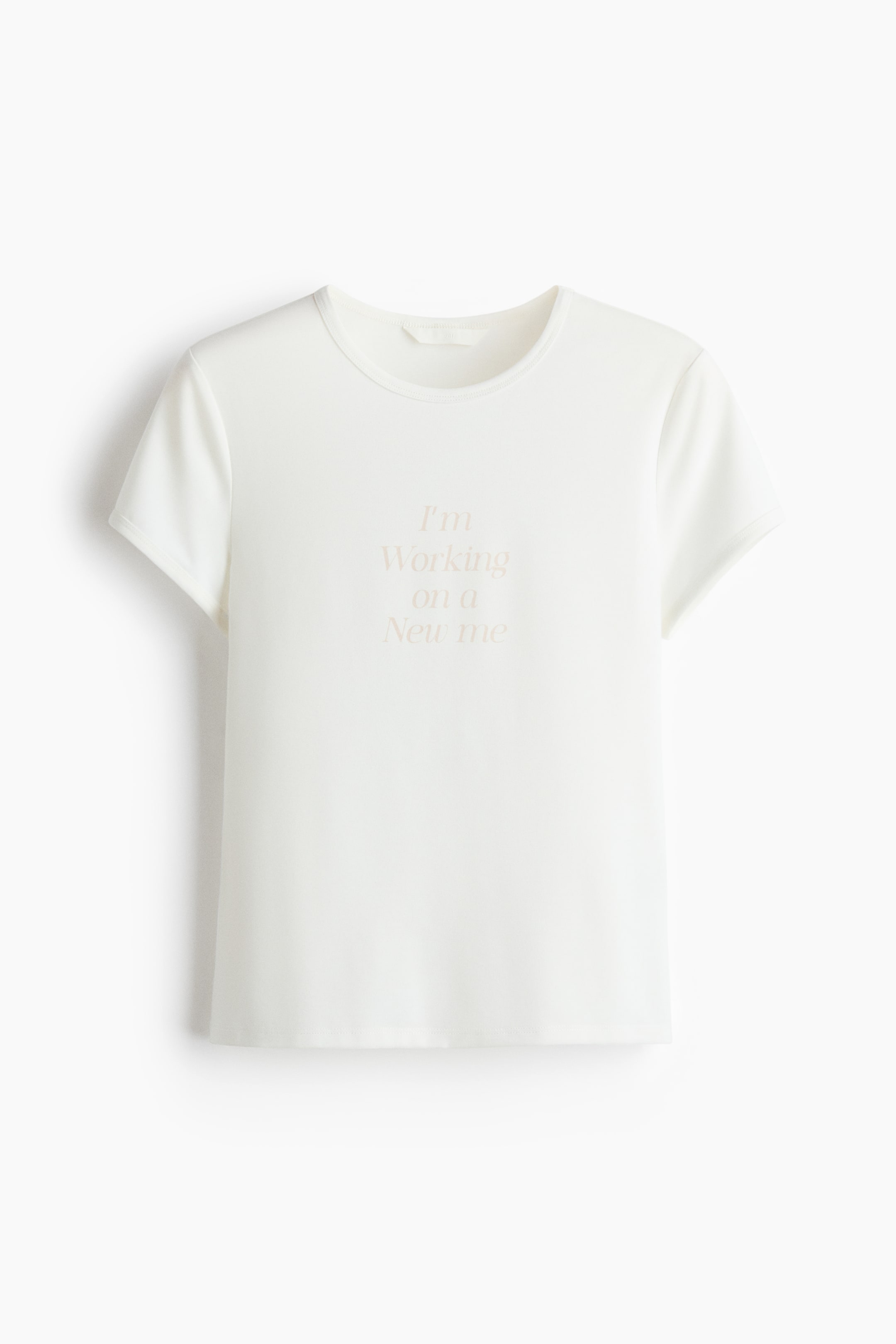 View larger image: A fitted, off-white jersey t-shirt is presenting its front view, featuring a round neckline, short sleeves, and a straight-cut hem. The chest is displaying a light beige printed text motif that reads, 'I'm Working on a New me'.