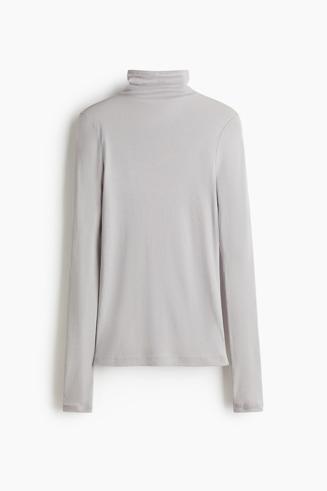 Un top grigio chiaro in morbido jersey di cotone pima presenta la parte anteriore, caratterizzato da un collo alto e maniche extra lunghe. - 1