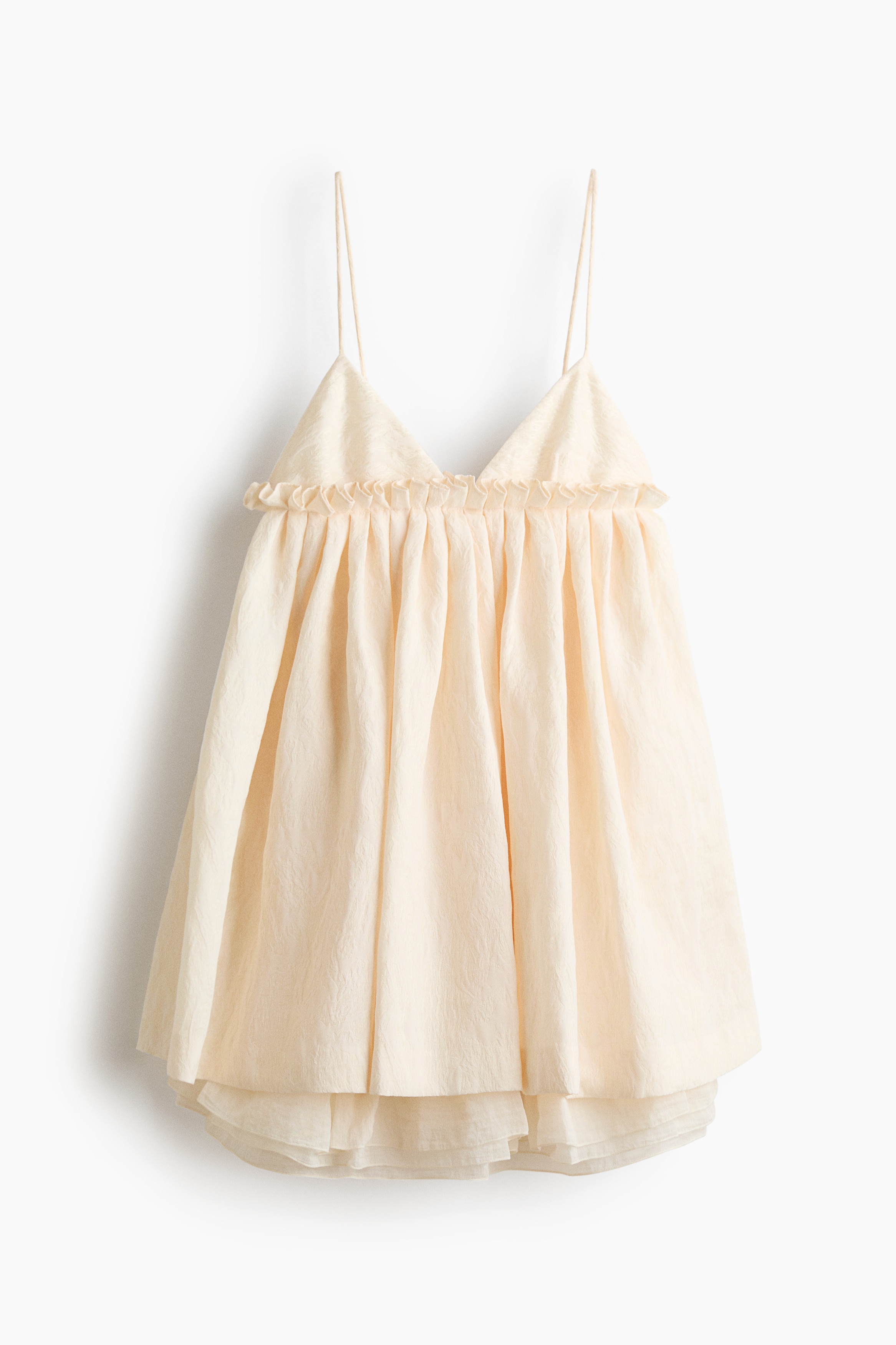 Une robe Ã©vasÃ©e Ã  fines bretelles de couleur crÃ¨me, en tissu jacquard, est portÃ©e par le mannequin. Elle prÃ©sente un dÃ©colletÃ© en V avec de dÃ©licates bonnets bordÃ©s de dentelle et de fines bretelles spaghetti. La robe comporte une couture volantÃ©e et plissÃ©e sous la poitrine qui sâÃ©panouit en une jupe Ã©vasÃ©e.