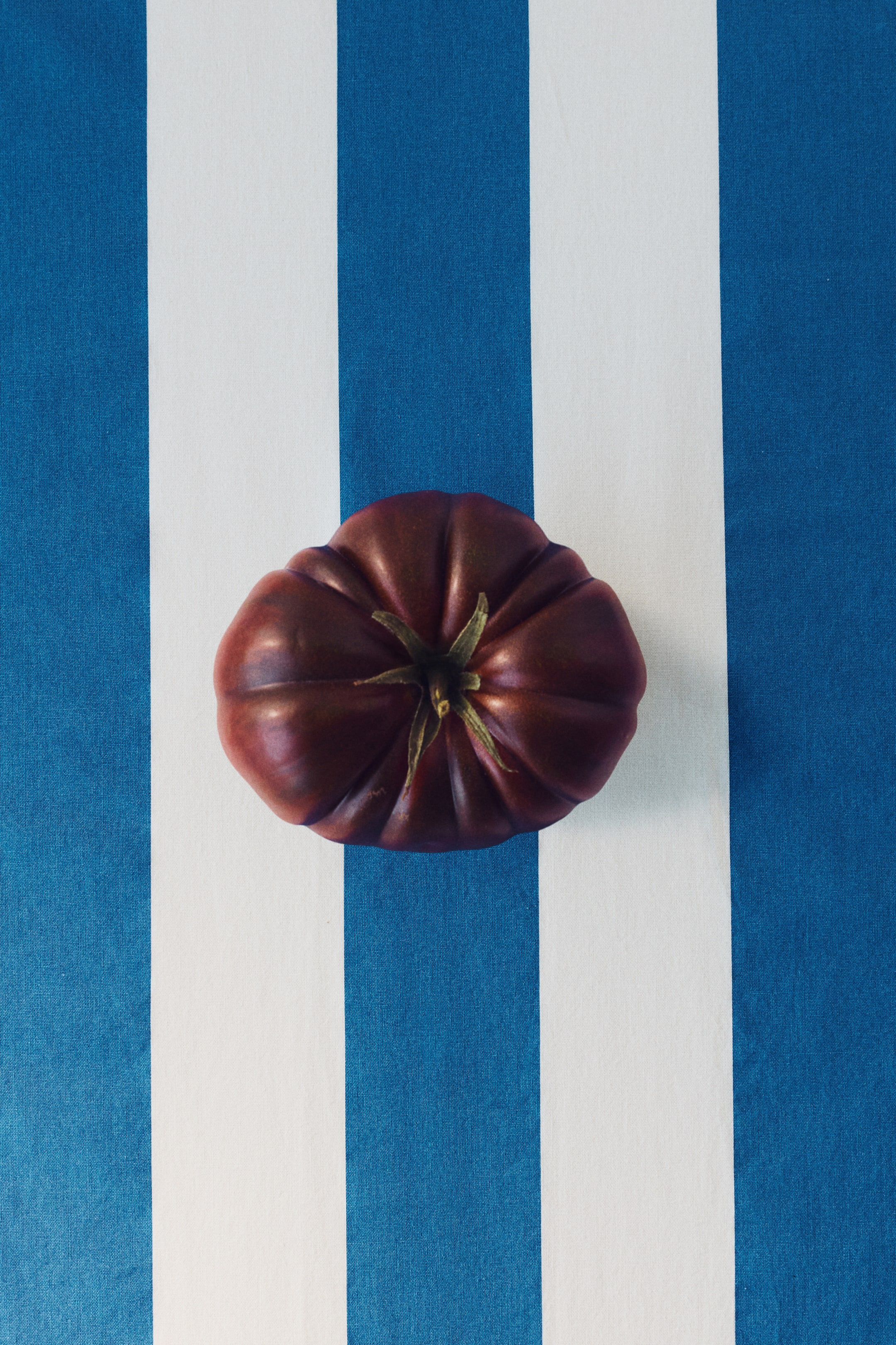 View larger image: A deep red, lobed tomato showcases its ribbed surface and a green star-shaped calyx from an overhead perspective.