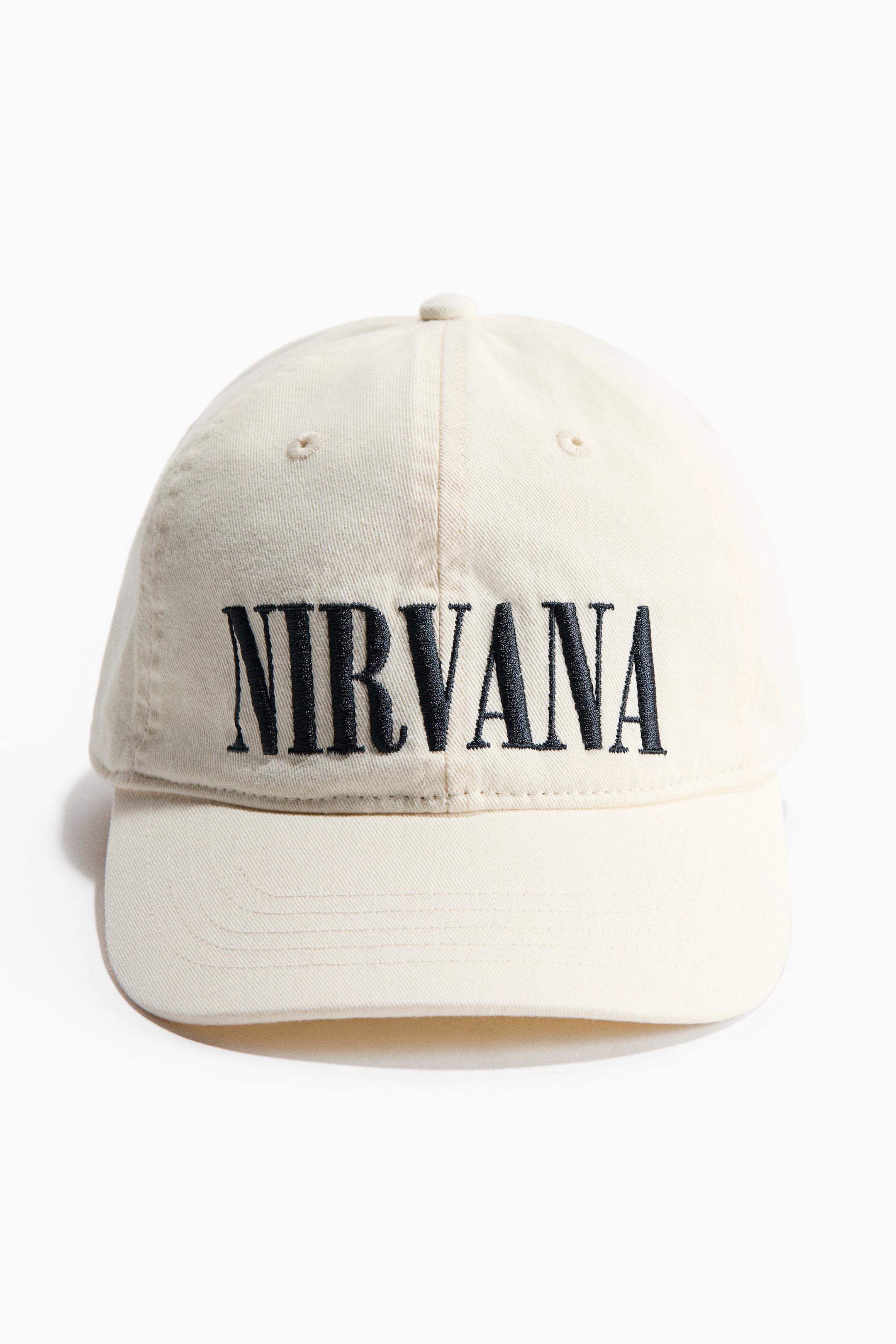 View larger image: A cream baseball cap is facing forward, with "NIRVANA" embroidered in black across its soft crown. It features a curved brim, ventilation eyelets, and a top button.